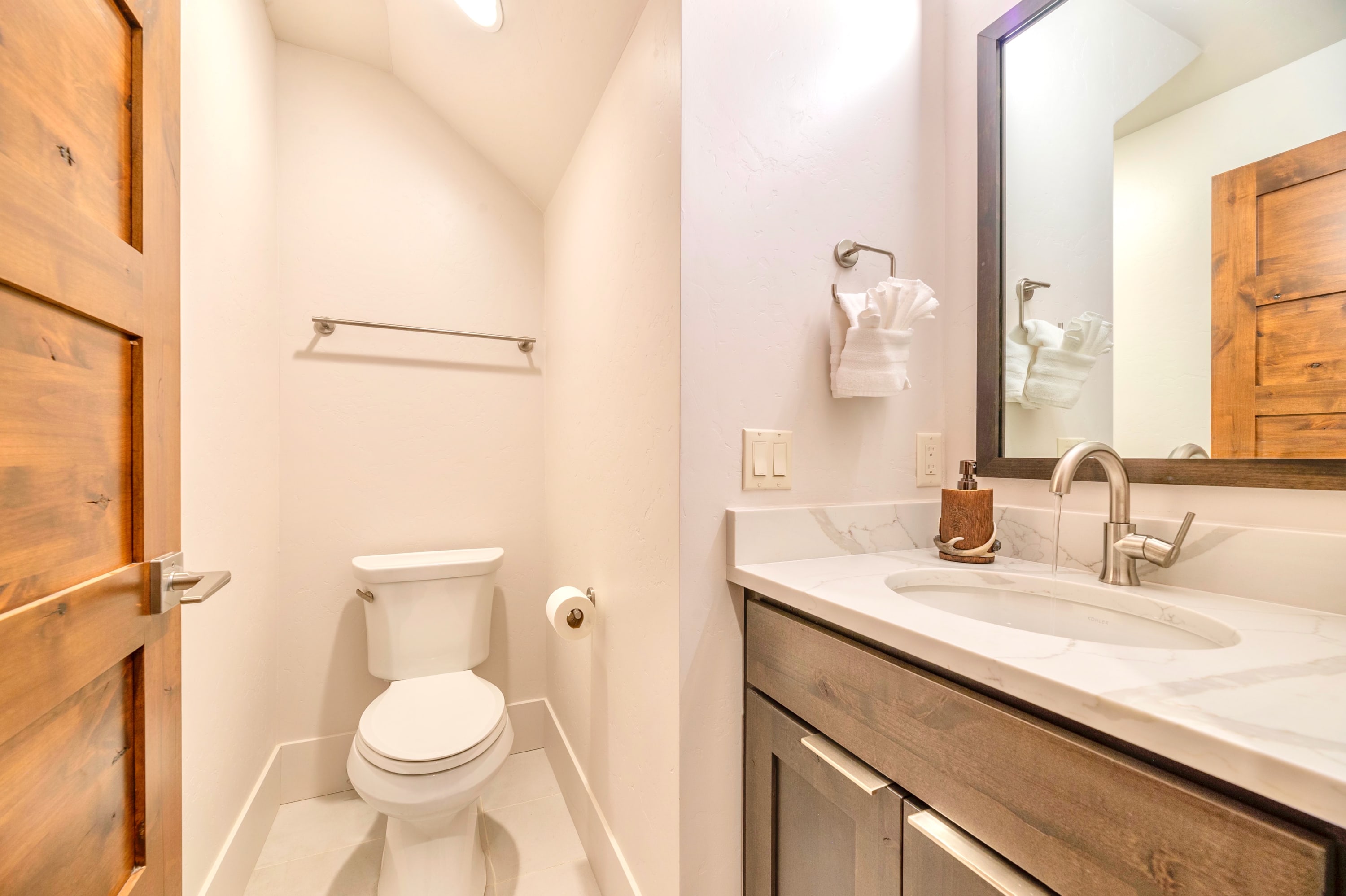 Compact half bathroom with a single vanity, white quartz countertop, and dark wood cabinet, featuring a large mirror and a separate alcove for the toilet.