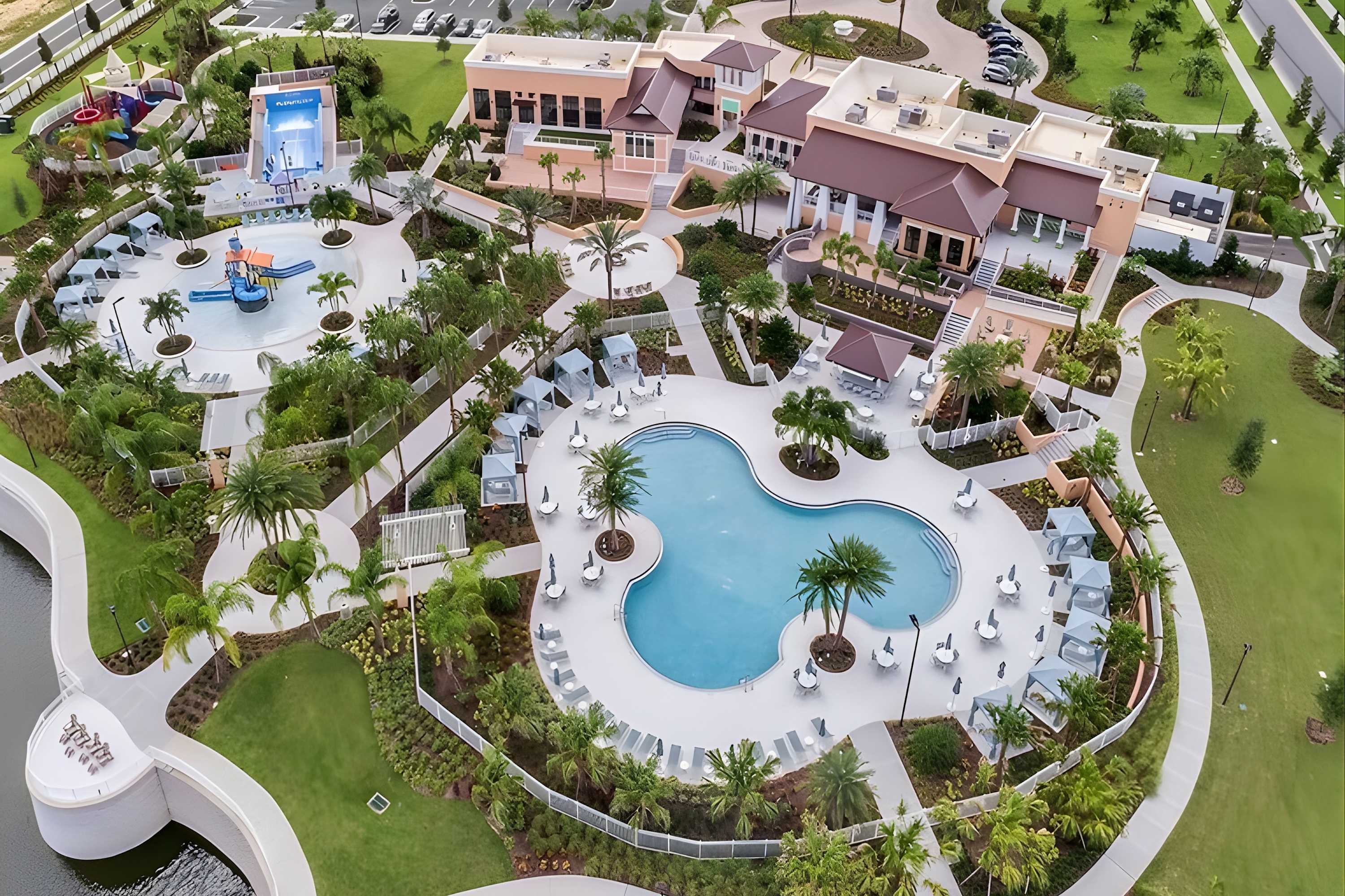 Aerial view of a large resort-style communal pool area featuring multiple swimming pools, lounge chairs, cabanas, and surrounding buildings with lush tropical landscaping.