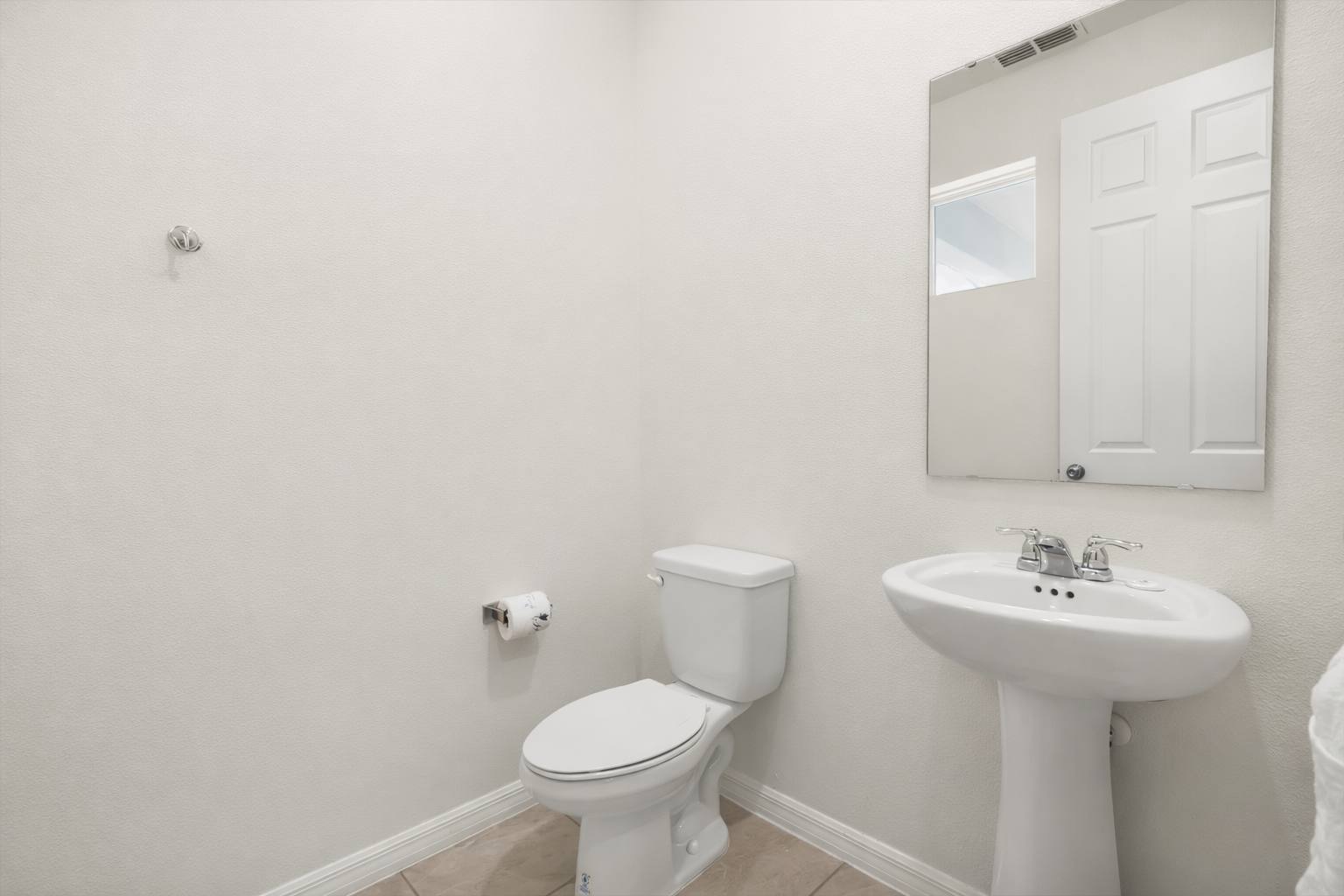 Simple and clean half bathroom featuring a white pedestal sink with a chrome faucet, a toilet, and a rectangular mirror above the sink, all against light-colored walls.