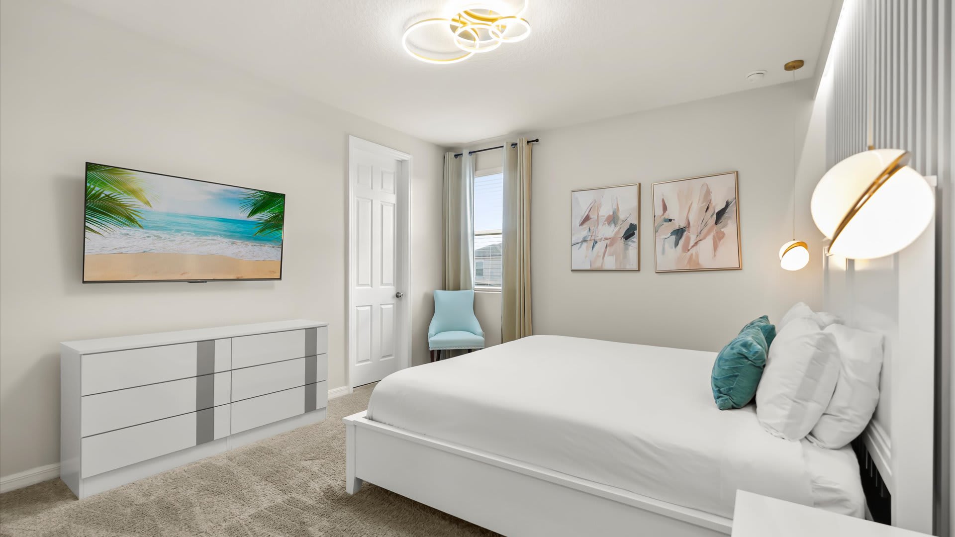 Bright bedroom with light gray walls, a white bed frame, and a white dresser. A large wall-mounted TV displays a beach scene, and a modern circular chandelier hangs from the ceiling. A light blue accent chair is visible by the window.