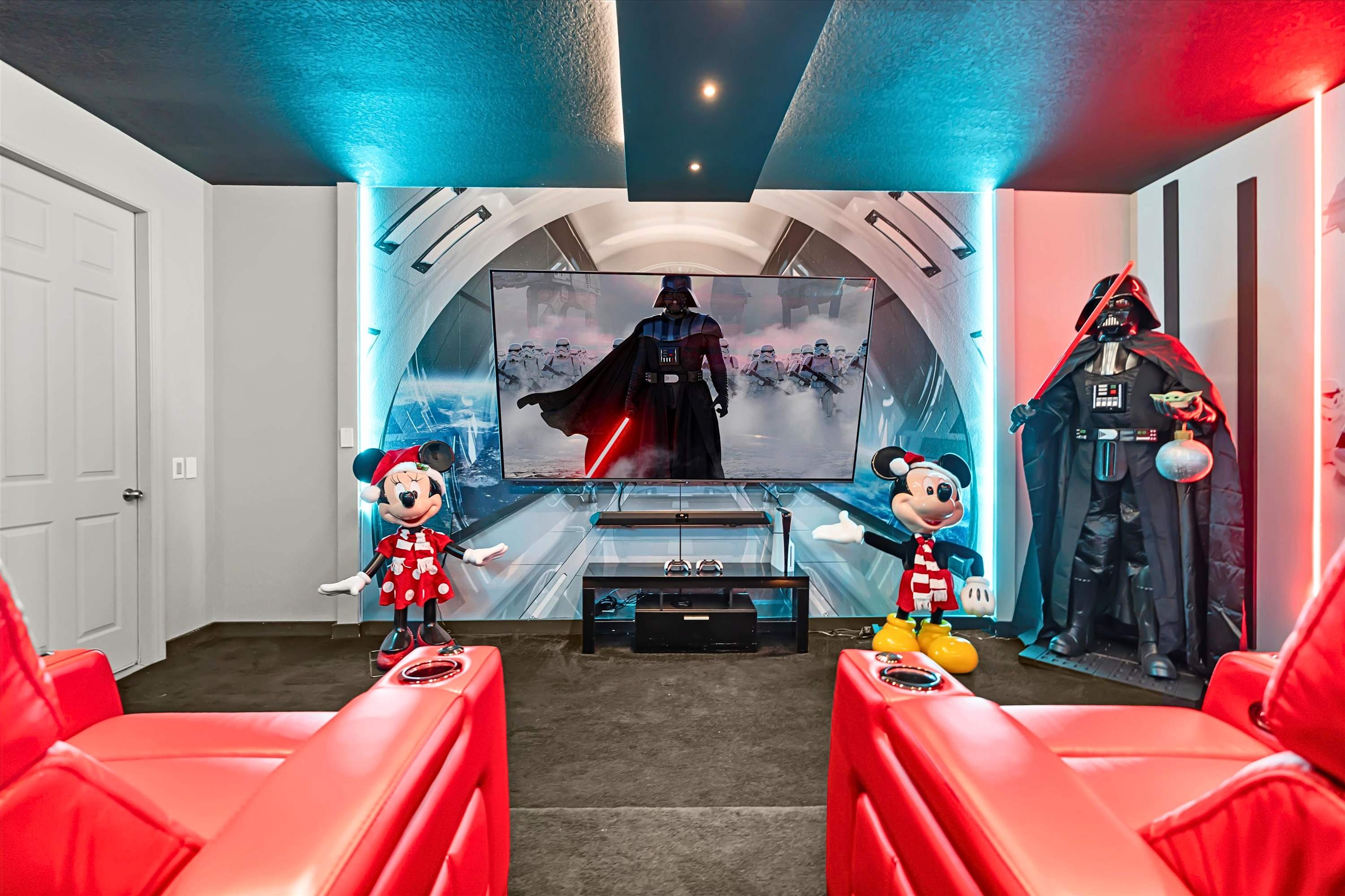 The Star Wars-themed media room features a large wall-mounted TV displaying Darth Vader, flanked by Mickey and Minnie Mouse statues and a life-sized Darth Vader figure. Red leather recliners are visible in the foreground, with blue and red LED strip lighting illuminating the walls.