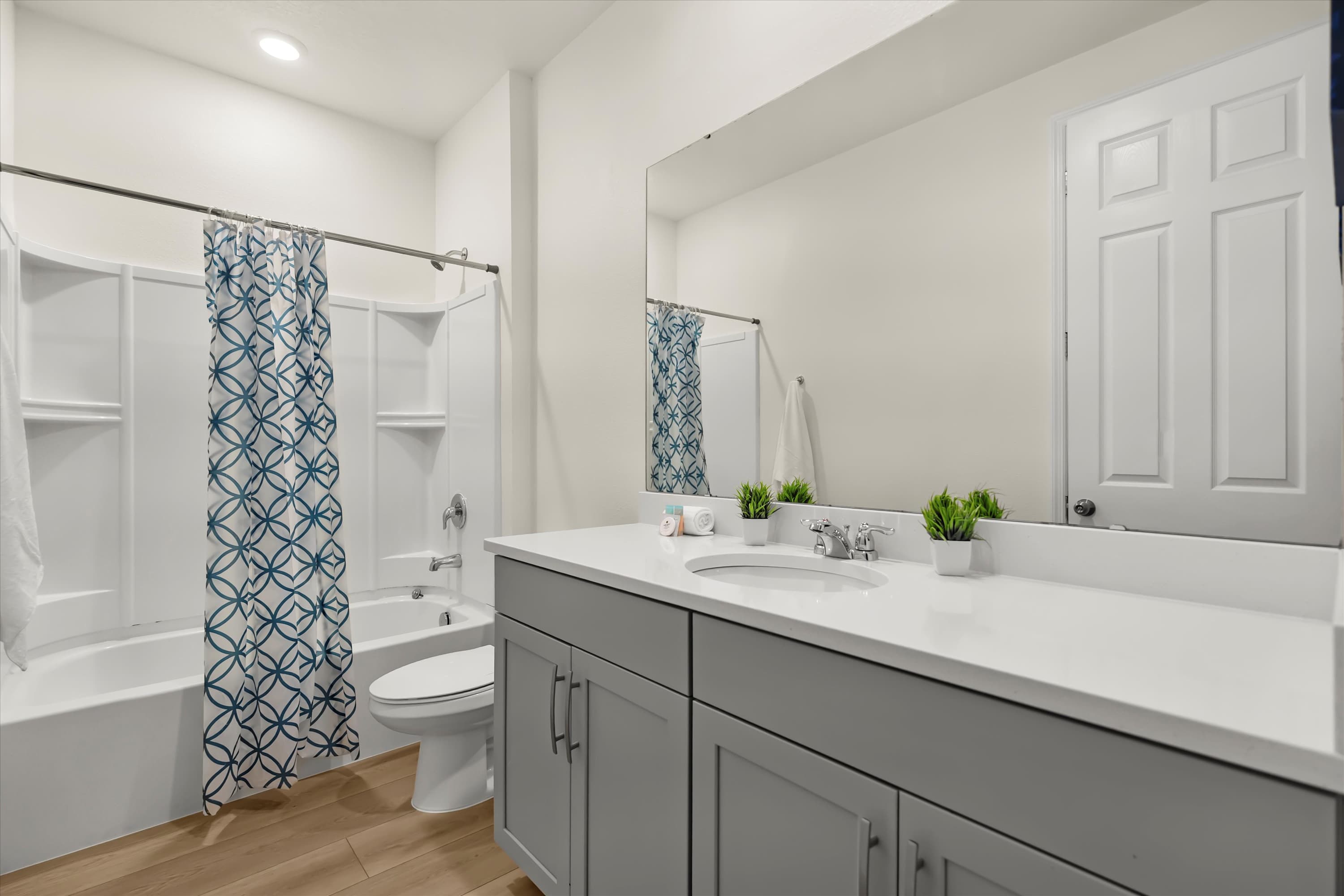Bright bathroom with a single gray vanity, white countertop, and a white shower/tub combo with a blue and white patterned curtain.