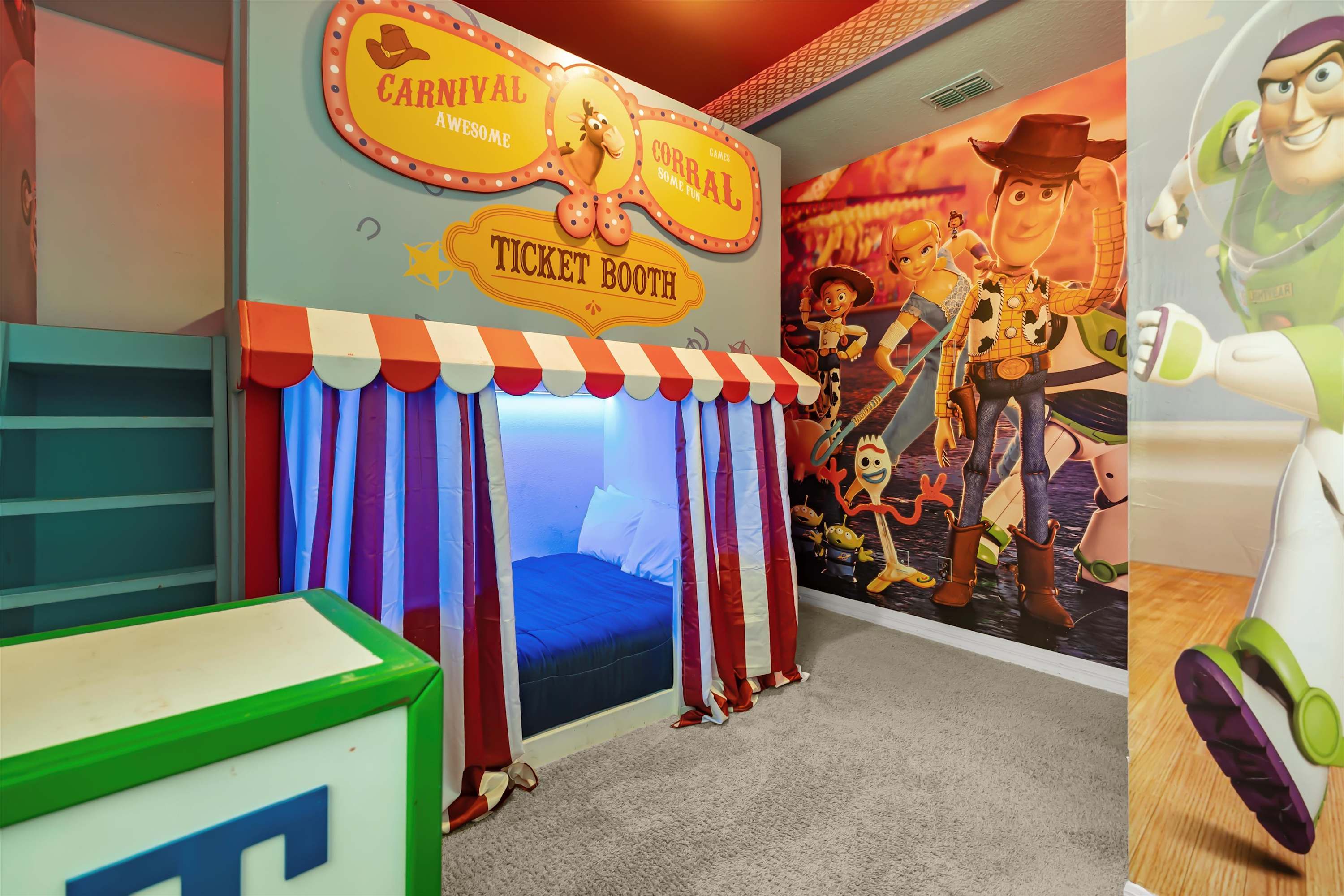 Toy Story themed bedroom featuring a carnival-style bed enclosure with red and white striped curtains, a "Ticket Booth" sign, and a large wall mural of Woody, Buzz, and other characters.