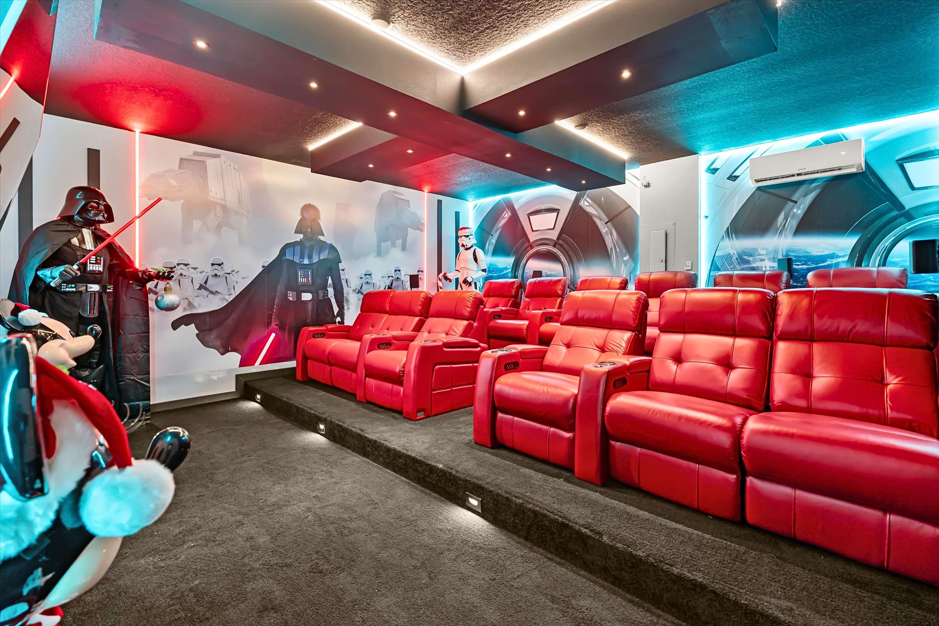 Immersive Star Wars-themed media room with tiered rows of red reclining theater seats, a large projection screen, and walls decorated with Darth Vader and stormtrooper murals, illuminated by red and blue accent lighting.