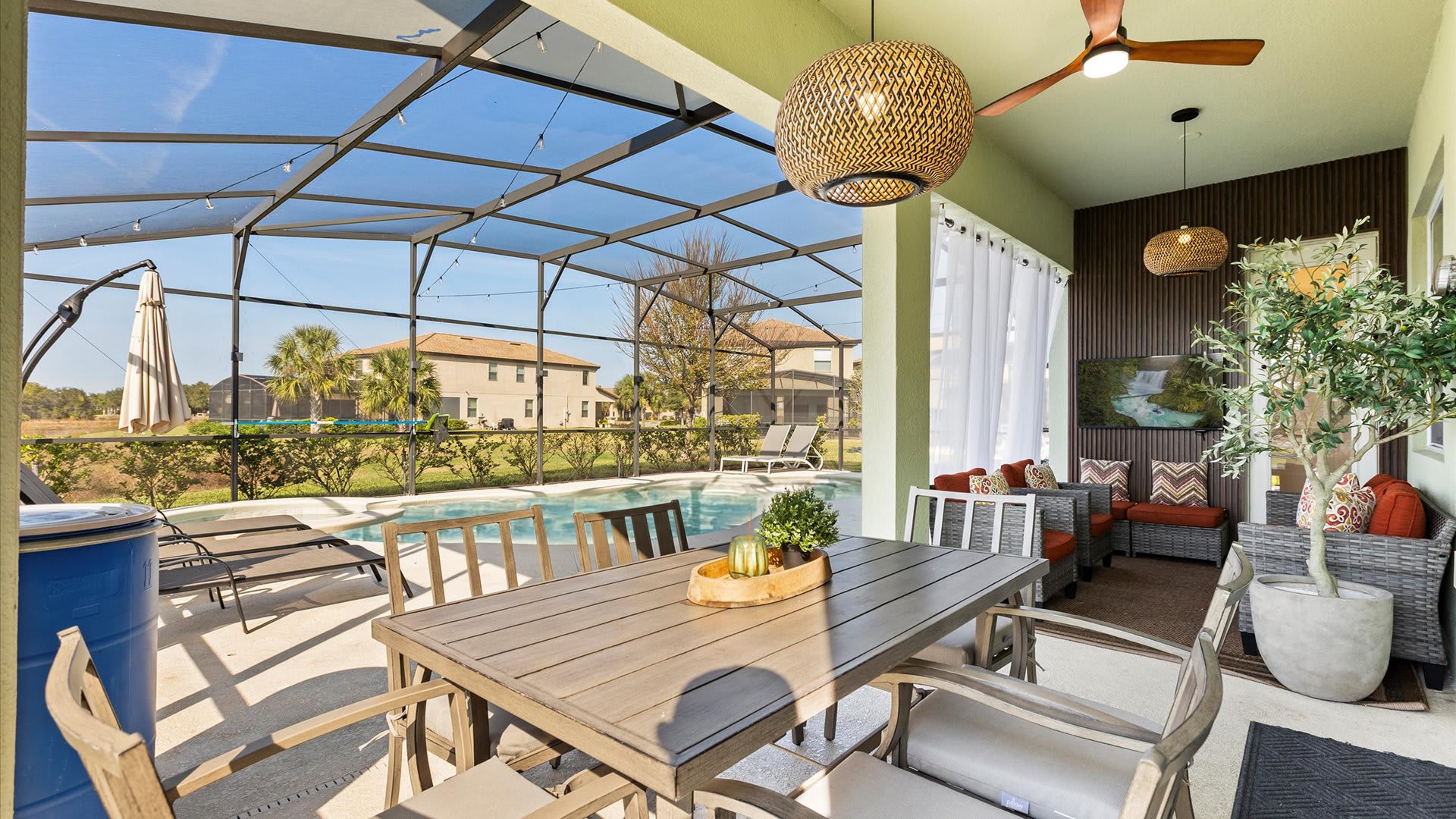 Inviting covered patio area with an outdoor dining table and a comfortable seating arrangement, complete with a ceiling fan and decorative lighting, overlooking the private screened pool.