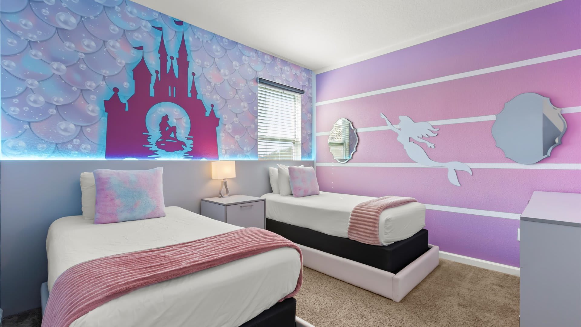 Themed bedroom with two twin beds, featuring a vibrant purple and blue wall mural depicting a mermaid and castle silhouette with integrated LED lighting. A mermaid cutout adorns the adjacent purple striped wall.