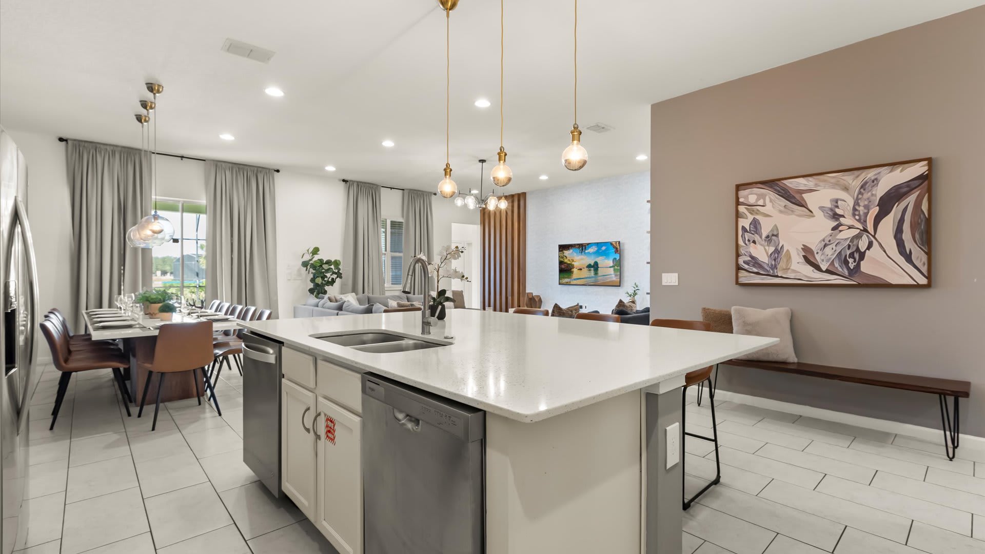 An expansive view of the open-concept living space, showcasing the kitchen island with bar seating, leading into the dining area and living room beyond. The light tile flooring unifies the space, with modern pendant lights illuminating the kitchen.