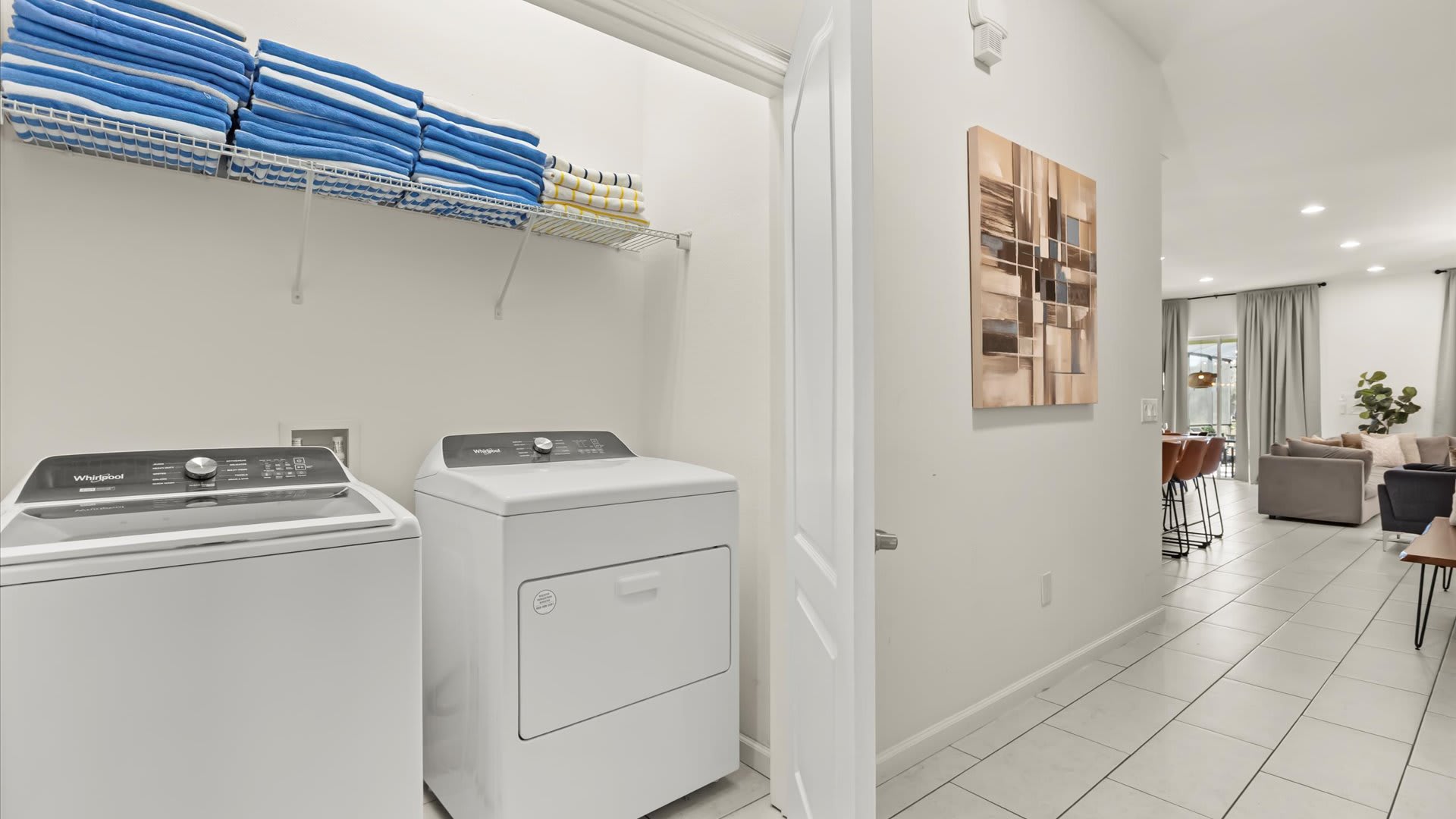 Functional laundry area equipped with a white top-load washing machine and a front-load dryer, with a wire shelf above stacked with blue and white towels.