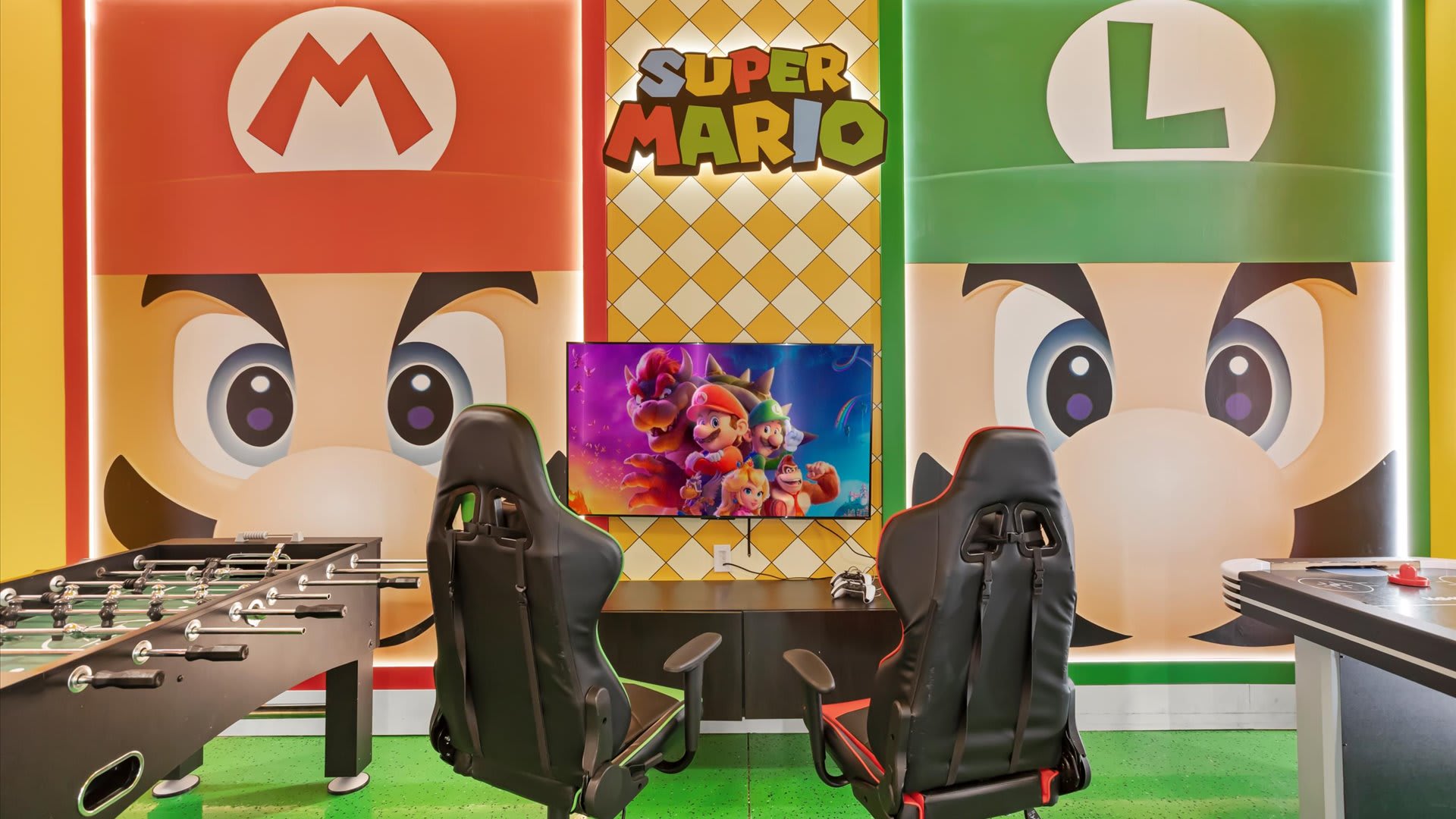 Close-up of the Super Mario-themed gaming area within the game room, featuring two ergonomic gaming chairs facing a large flat-screen TV, flanked by vibrant Mario and Luigi character murals.