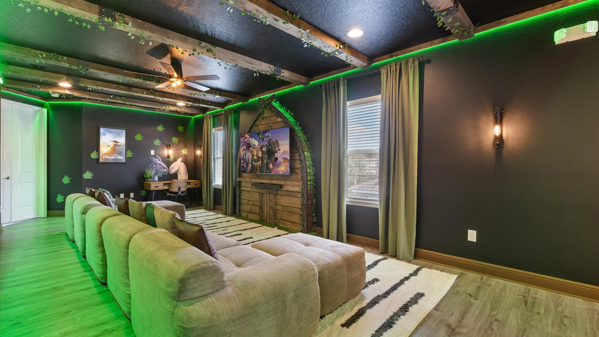 A dark-walled media room with a "How to Train Your Dragon" theme features a large L-shaped sectional sofa, a wall-mounted TV, and green LED strip lighting accentuating wooden beams adorned with artificial vines.