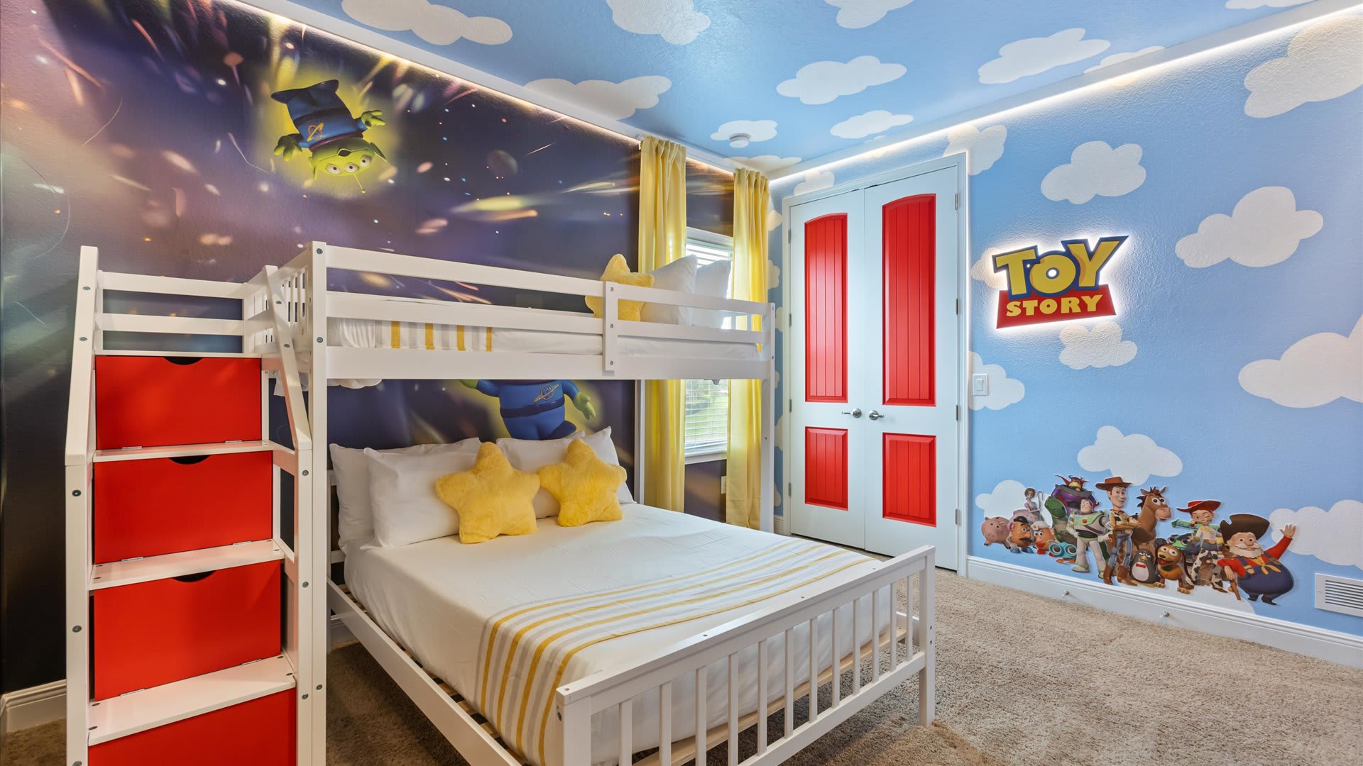 A wide shot of the Toy Story themed bedroom, featuring a white bunk bed with red storage drawers, a wall with the "Toy Story" logo and character decals, and cloud-painted ceiling.