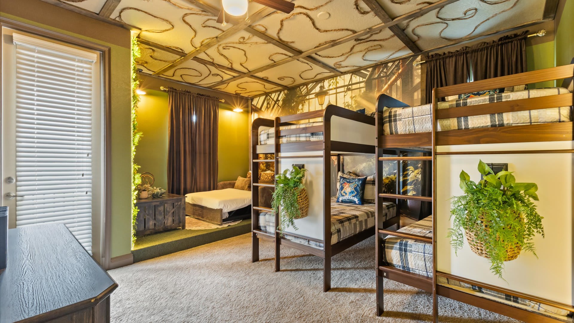 A uniquely themed bedroom featuring two wooden bunk beds with plaid bedding, a pull-out sofa, and a ceiling decorated with a whimsical vine pattern, creating a magical forest ambiance.