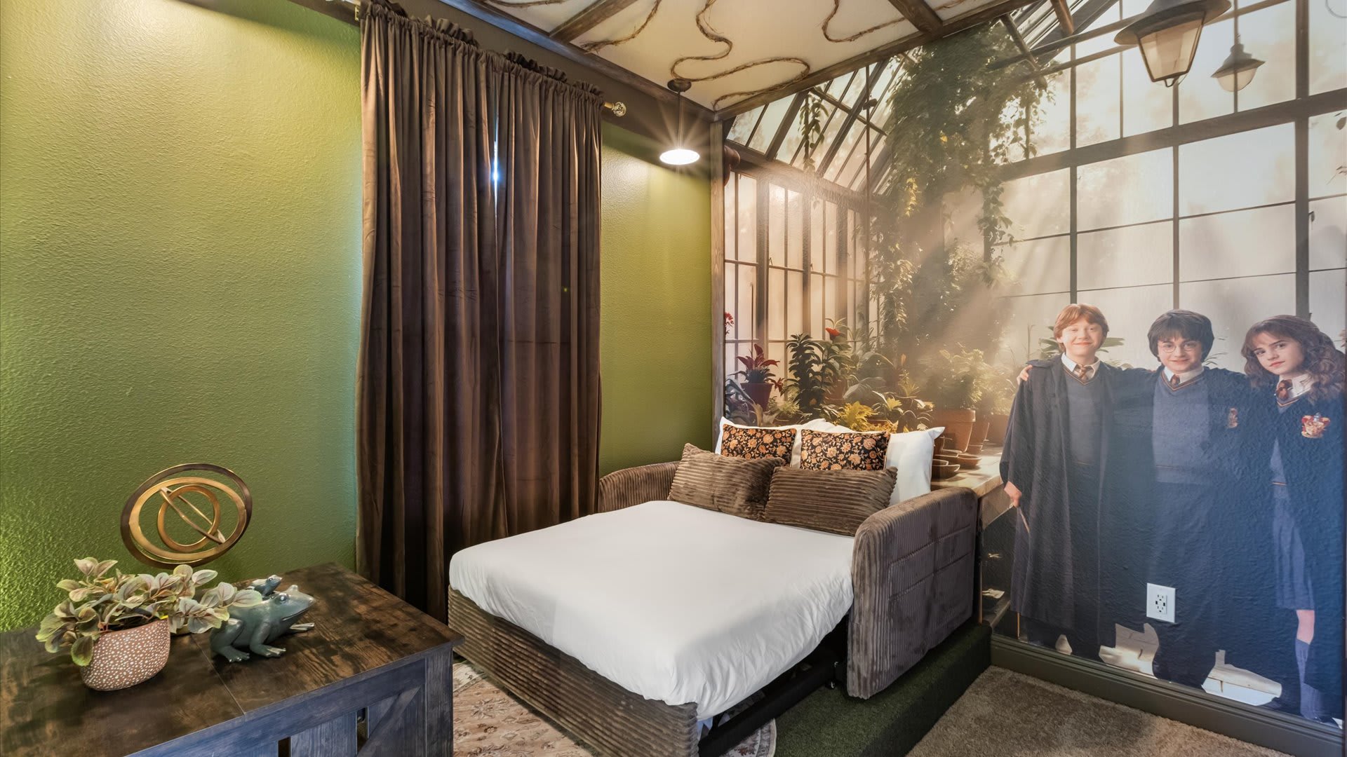 A corner of the themed bedroom featuring a pull-out sofa bed with decorative pillows, set against a large Harry Potter mural depicting characters in a greenhouse scene.