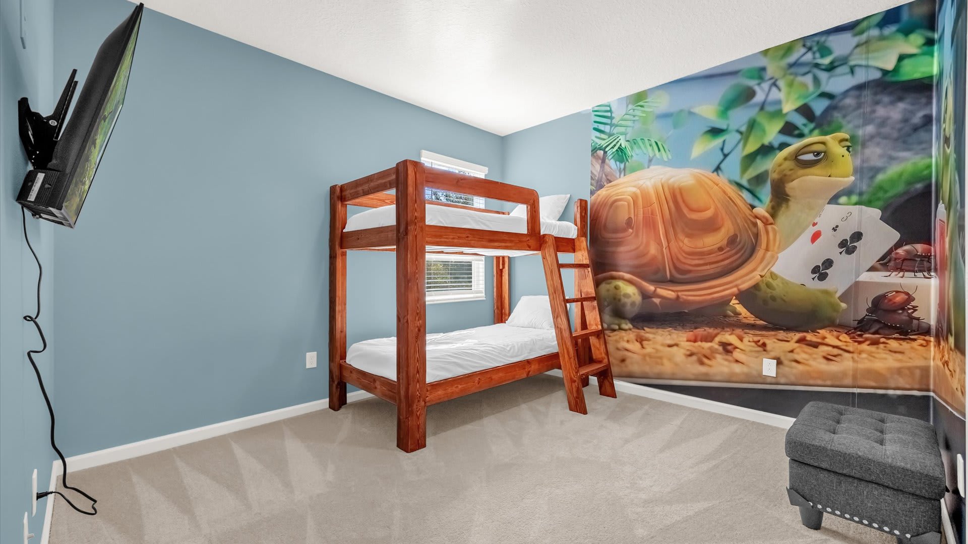 Playful bedroom with light blue walls and a large wall mural depicting a turtle playing cards, furnished with a wooden bunk bed and a wall-mounted television.