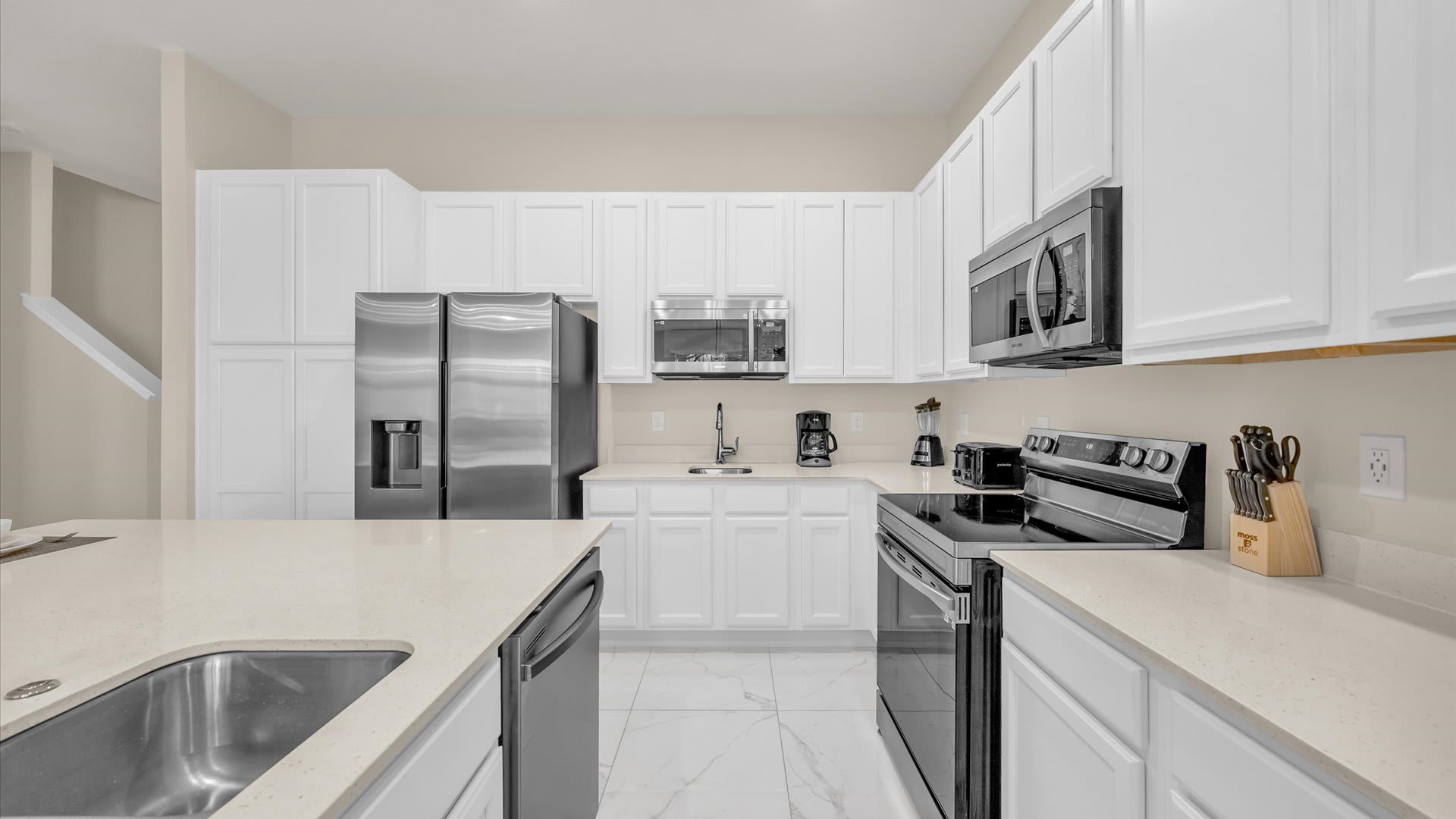 View of the modern kitchen showcasing white shaker cabinets, light quartz countertops, and black and stainless steel appliances including a stove, microwave, and refrigerator.