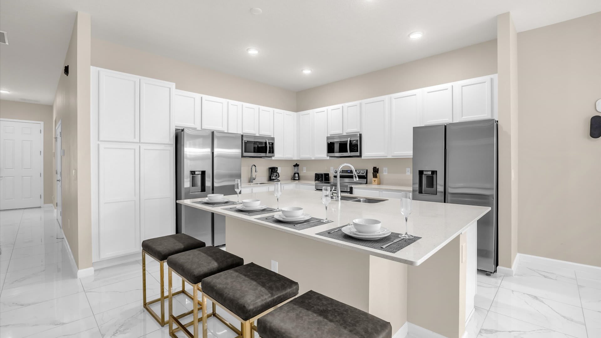 Modern kitchen with white shaker cabinets, light quartz countertops, stainless steel appliances, and a large island with three dark upholstered bar stools.
