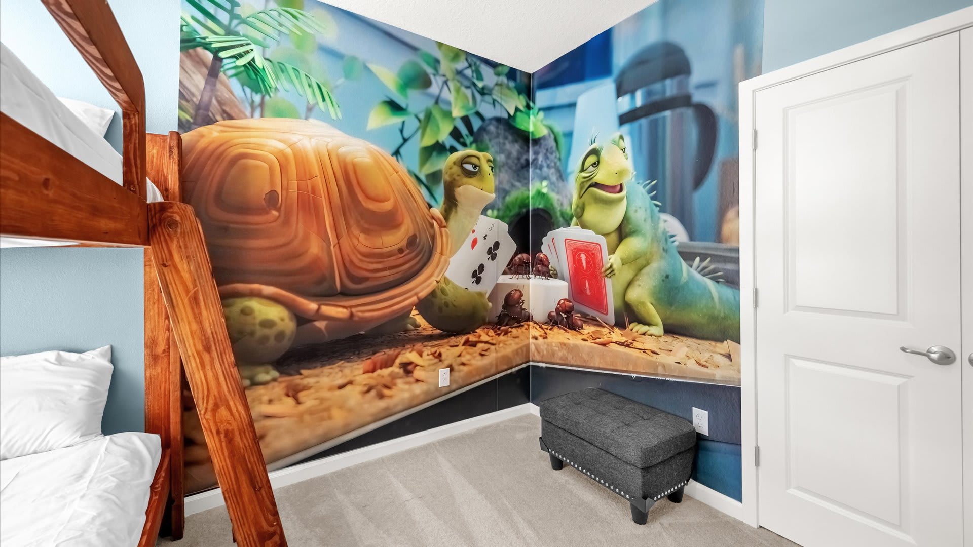 Corner view of a themed bedroom showcasing a vibrant wall mural of a turtle and an iguana playing cards, adjacent to a wooden bunk bed and a dark upholstered ottoman.