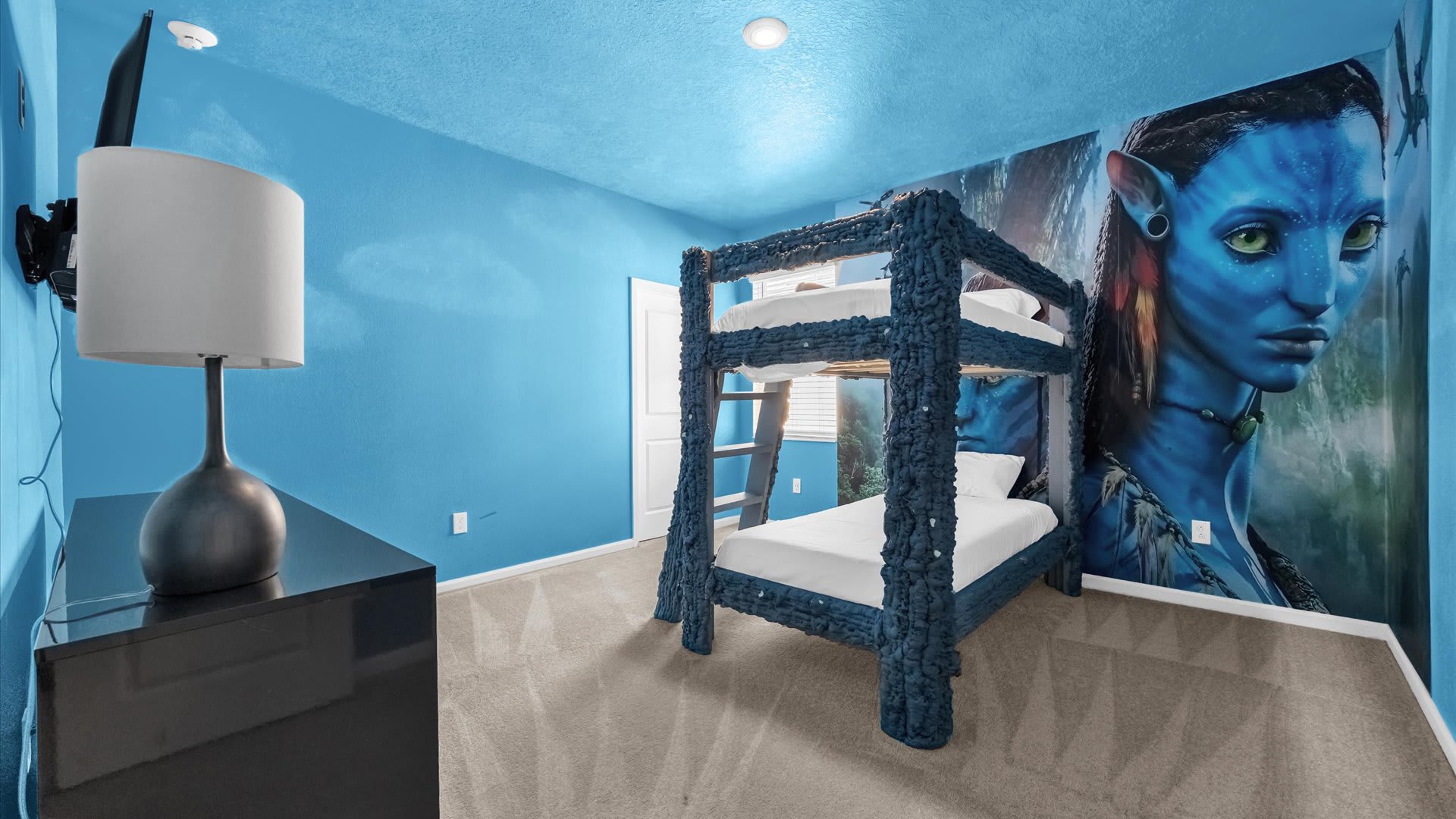 Vibrant blue bedroom featuring a large Avatar-themed wall mural, a unique blue textured bunk bed, a dark dresser with a lamp, and a wall-mounted TV.