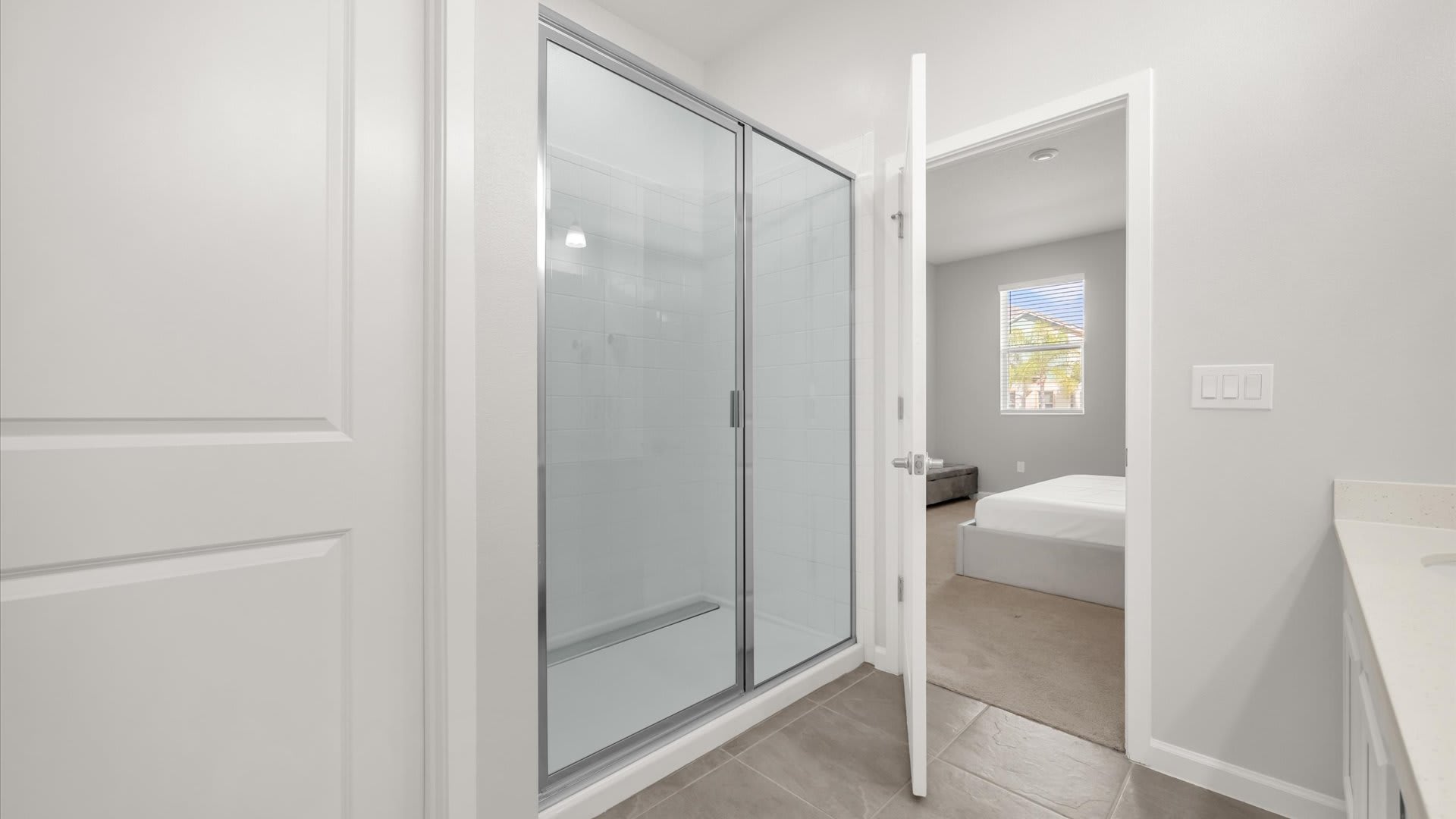 Modern walk-in shower with clear glass doors and white tiled walls, located within the en-suite bathroom. A doorway provides a view back into the master bedroom.