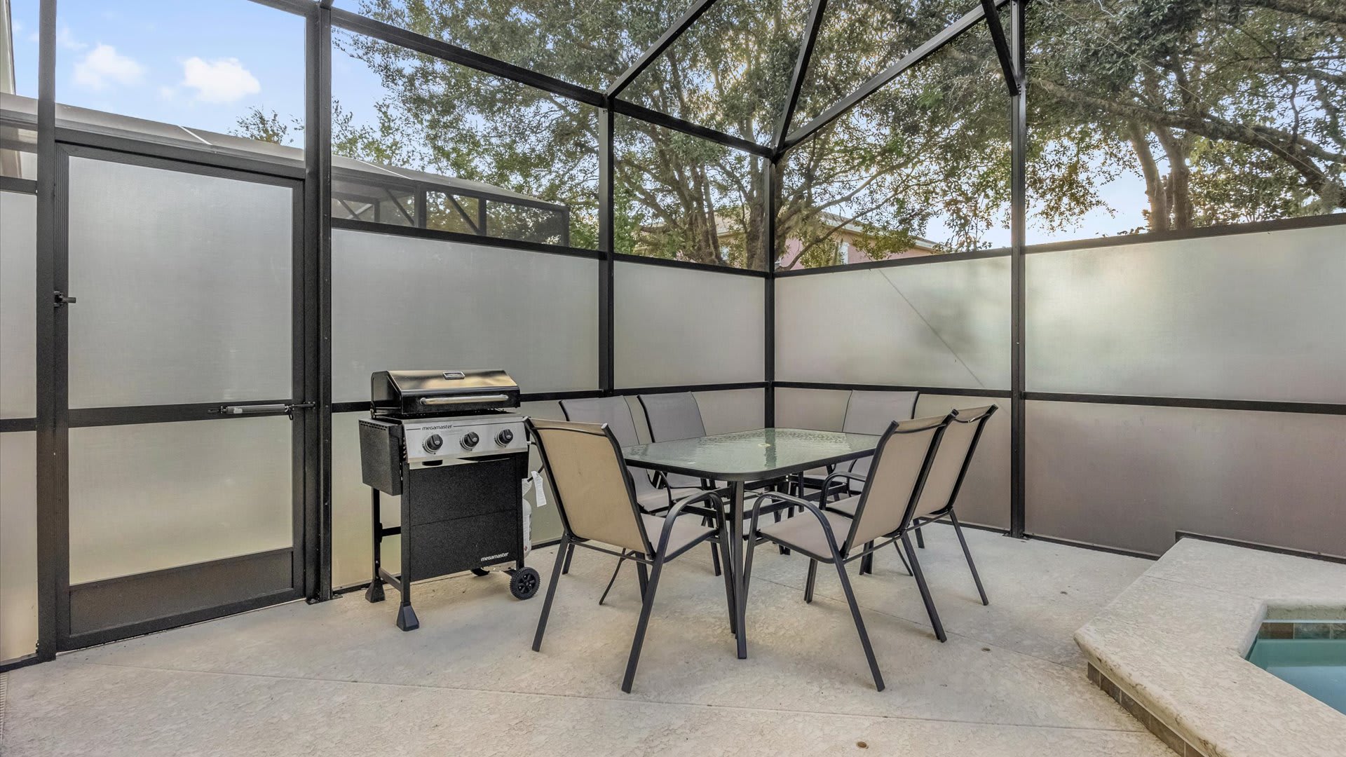 A dedicated outdoor dining and grilling area is situated within the screened pool enclosure, featuring a glass-top table with six chairs and a gas BBQ grill. Frosted privacy panels line the perimeter, providing a secluded space for al fresco meals.