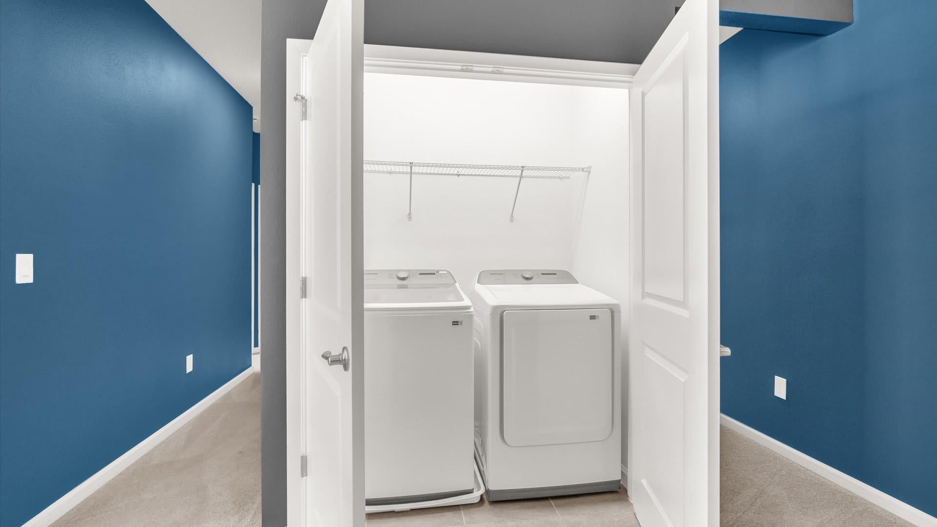 Functional laundry closet with bi-fold doors, equipped with a white top-loading washing machine and a matching dryer, and wire shelving for storage.