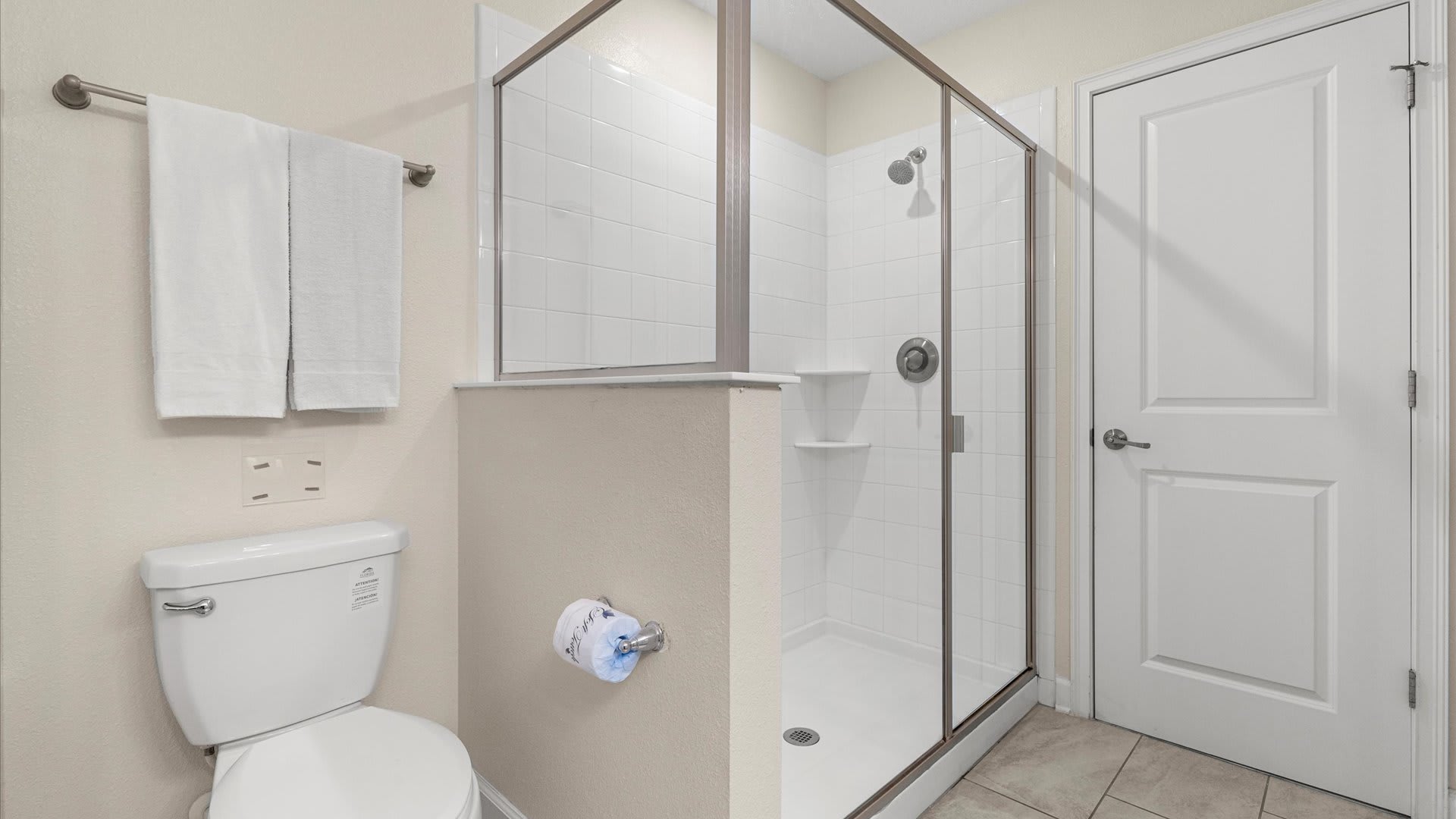 A clean bathroom featuring a white toilet and a spacious walk-in shower with a clear glass enclosure and white subway tiles.