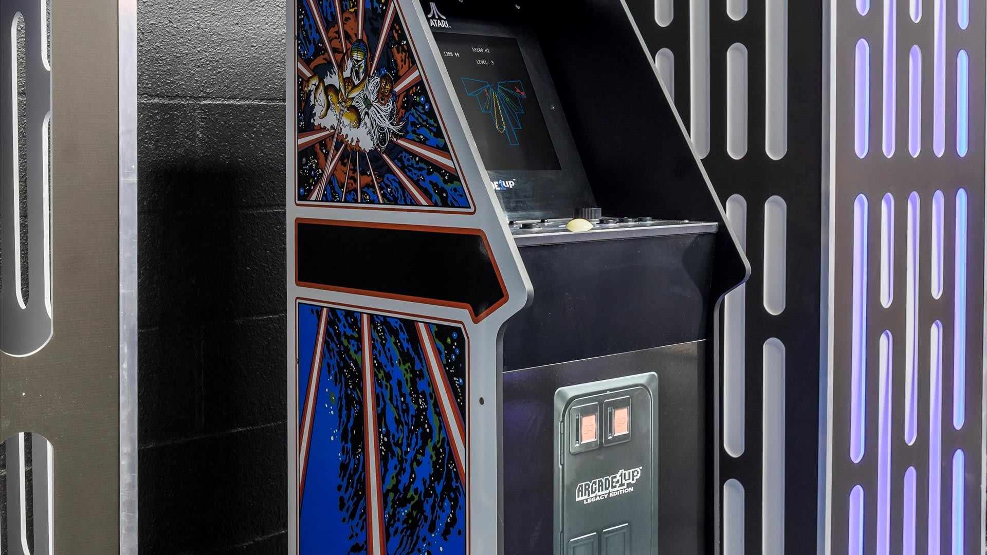 A vintage-style arcade game cabinet, featuring classic Atari artwork, stands against a dark wall with illuminated vertical panels, showcasing the "Centipede" game on its screen.