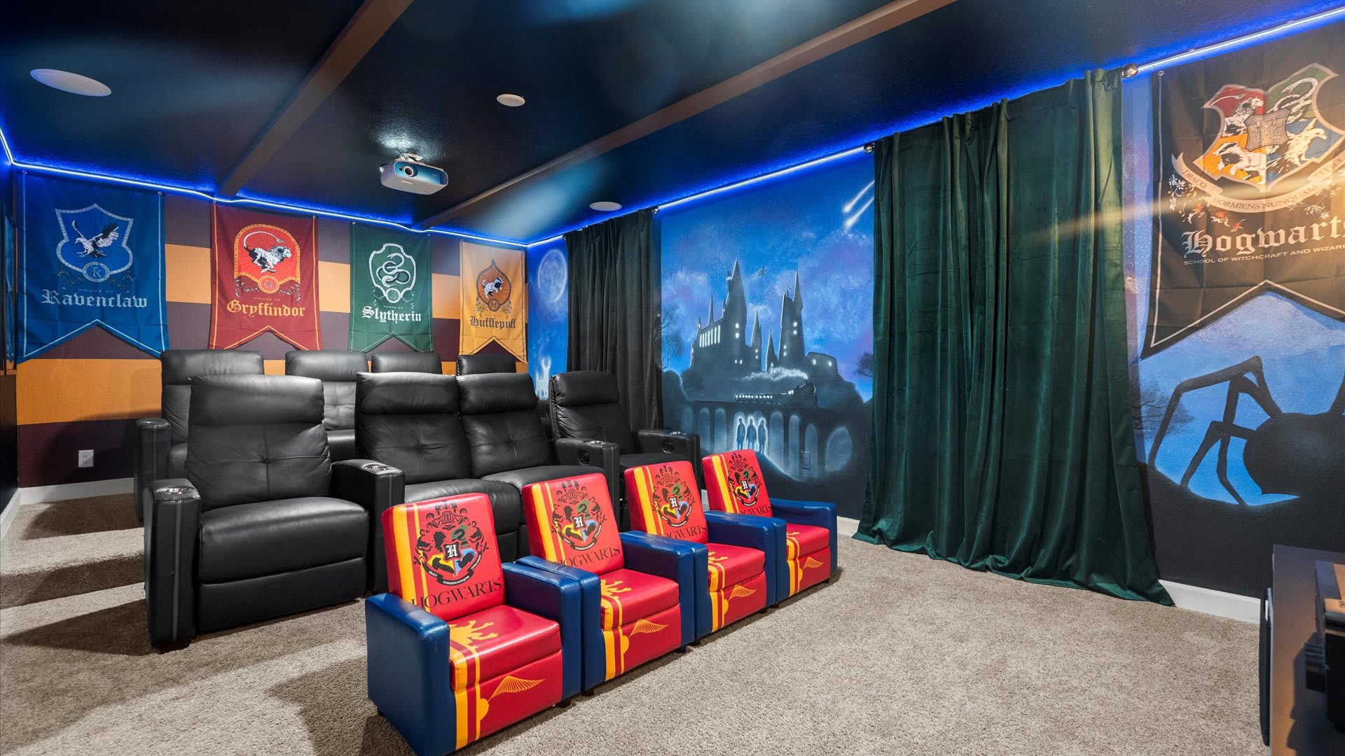 A Harry Potter-themed home cinema offers multiple rows of seating, including black recliners and red and blue themed chairs, with house banners and a Hogwarts mural adorning the walls under blue LED lighting.
