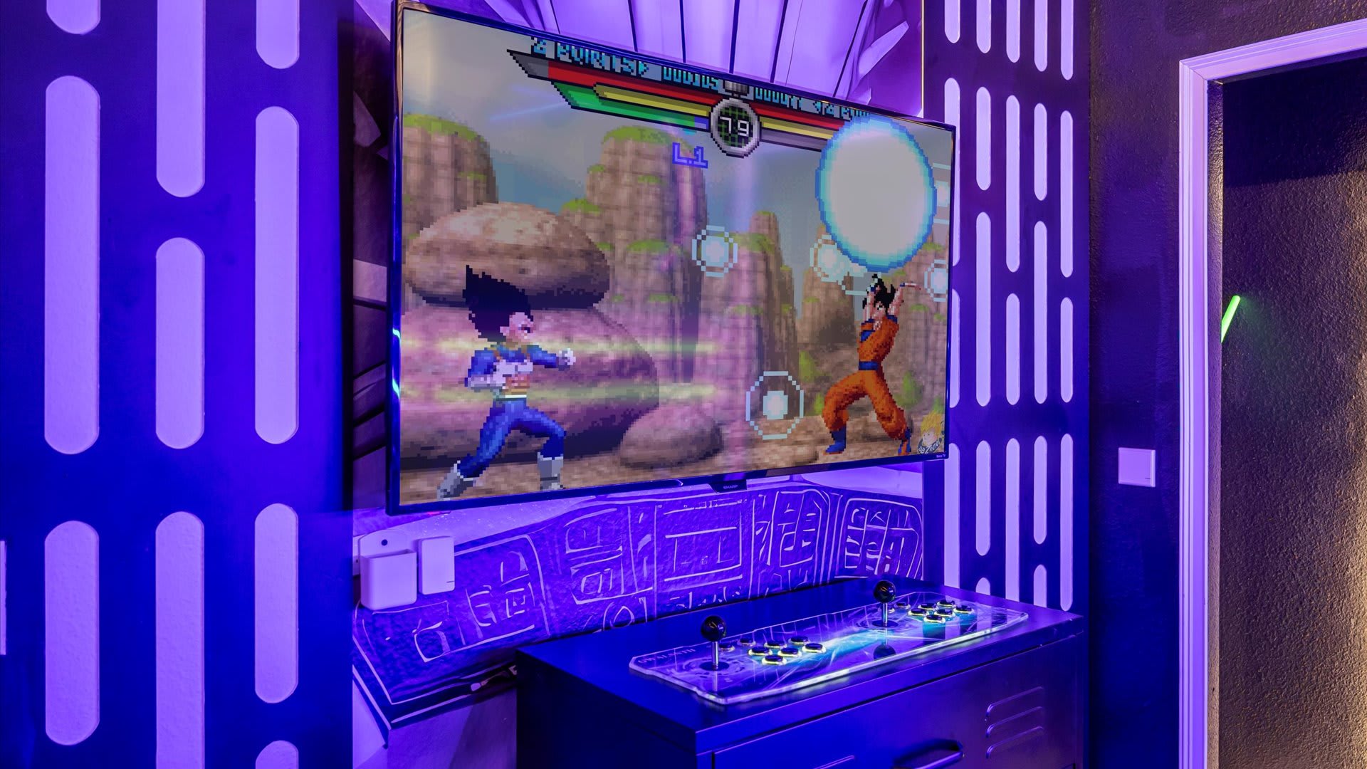 A vibrant game room featuring a large wall-mounted TV displaying a pixelated fighting game, an arcade controller setup, and walls adorned with Star Wars-inspired patterns and purple LED lighting.