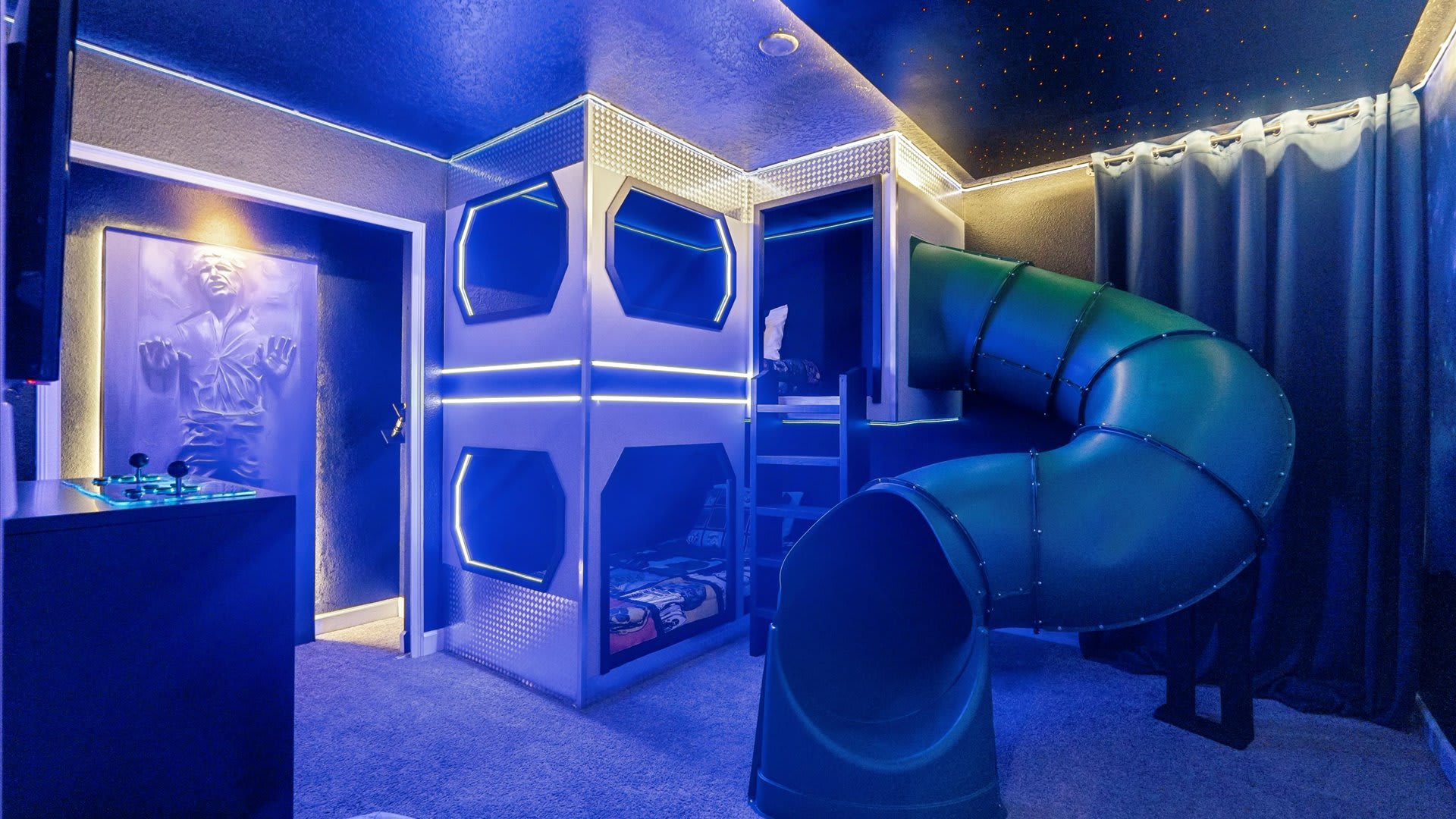 This Star Wars-themed bedroom includes a custom bunk bed with integrated lighting and a green slide, a Han Solo in carbonite door, and blue LED strip lighting, creating an immersive and playful atmosphere.