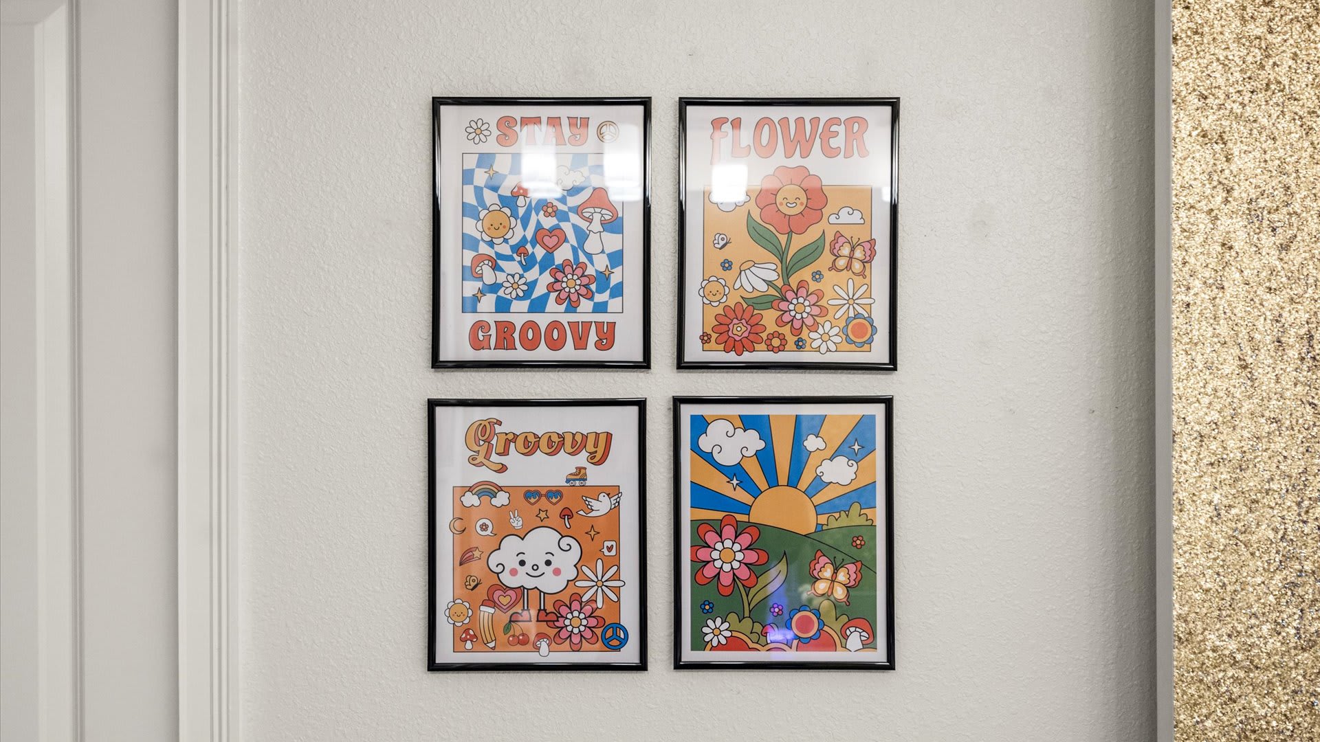 Four framed, colorful posters with groovy and floral designs, including "STAY GROOVY" and "FLOWER", arranged on a white wall, hinting at a vibrant, themed space.
