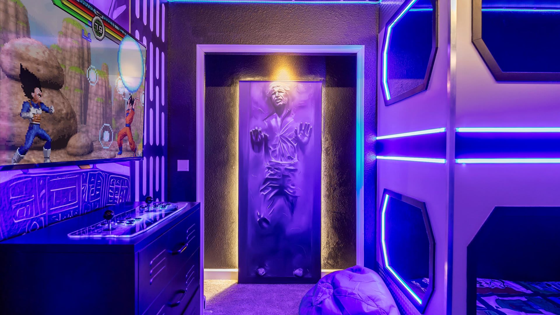 A themed entertainment space featuring a large TV with a fighting game, an arcade console, and a striking Han Solo in carbonite wall art next to futuristic bunk beds, all bathed in purple light.