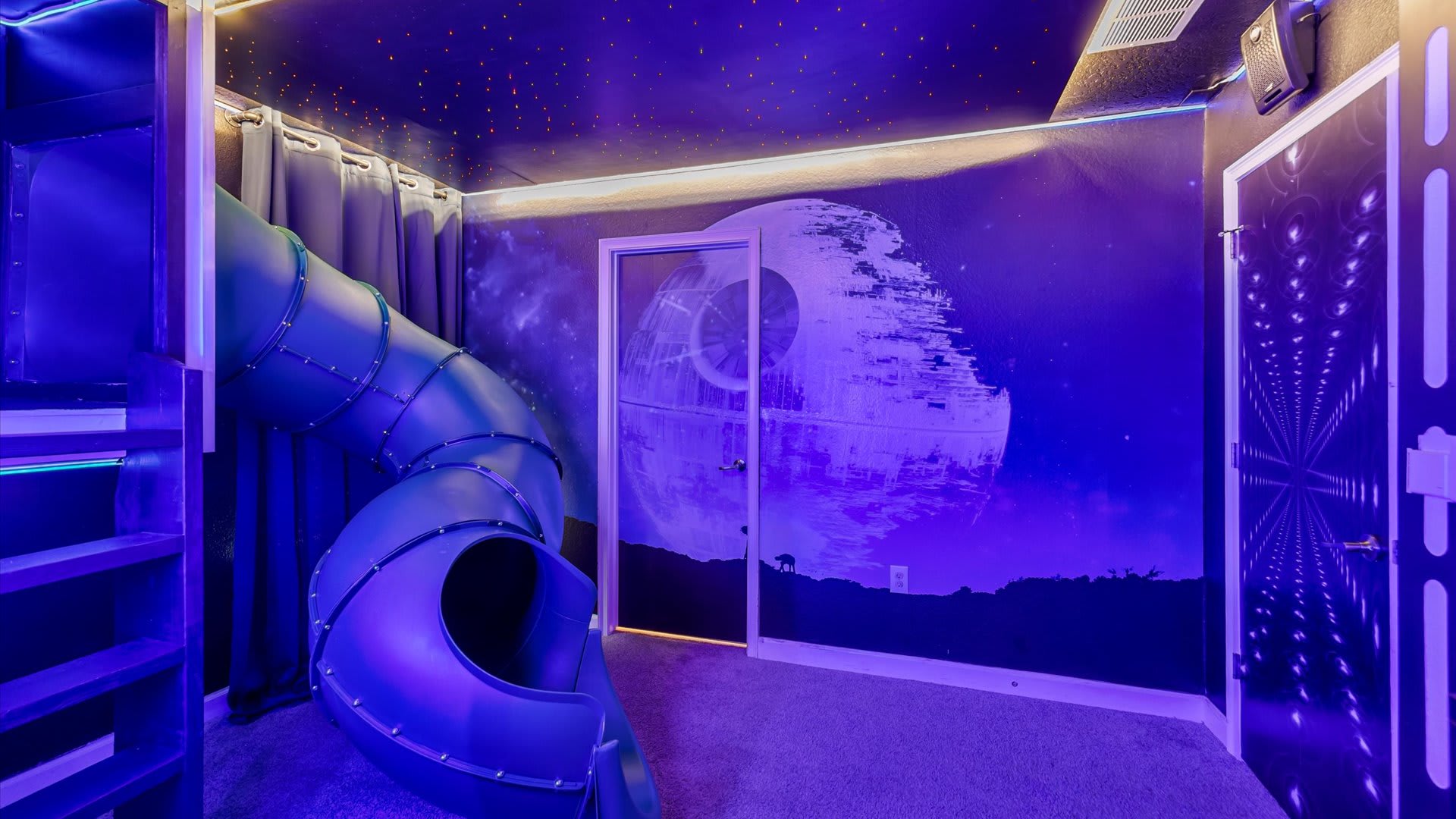 A vibrant Star Wars-themed bedroom featuring a large Death Star mural, a blue indoor slide, and bunk beds, all under a ceiling adorned with small star-like lights.