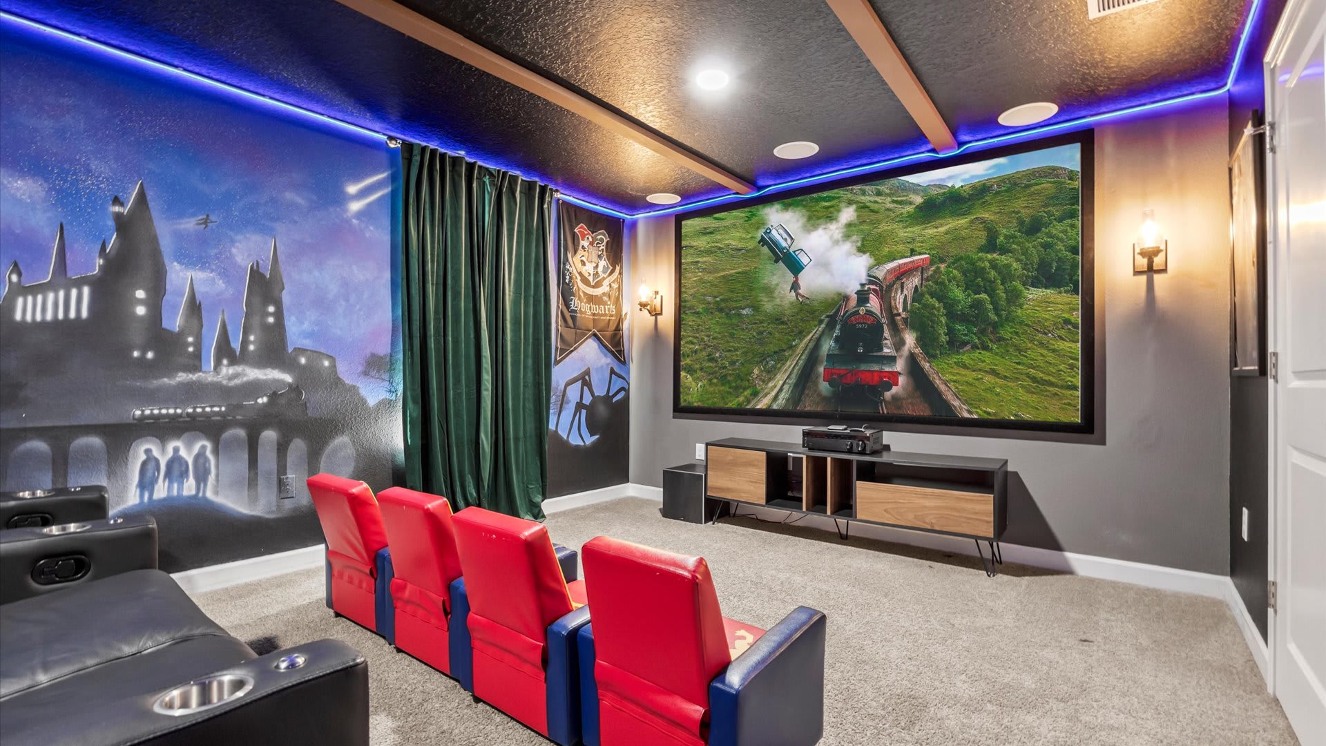 A Harry Potter-themed home cinema features a large projection screen displaying a scene from the movie, with a row of red and blue themed chairs in front of black recliners, and a Hogwarts mural on the wall.