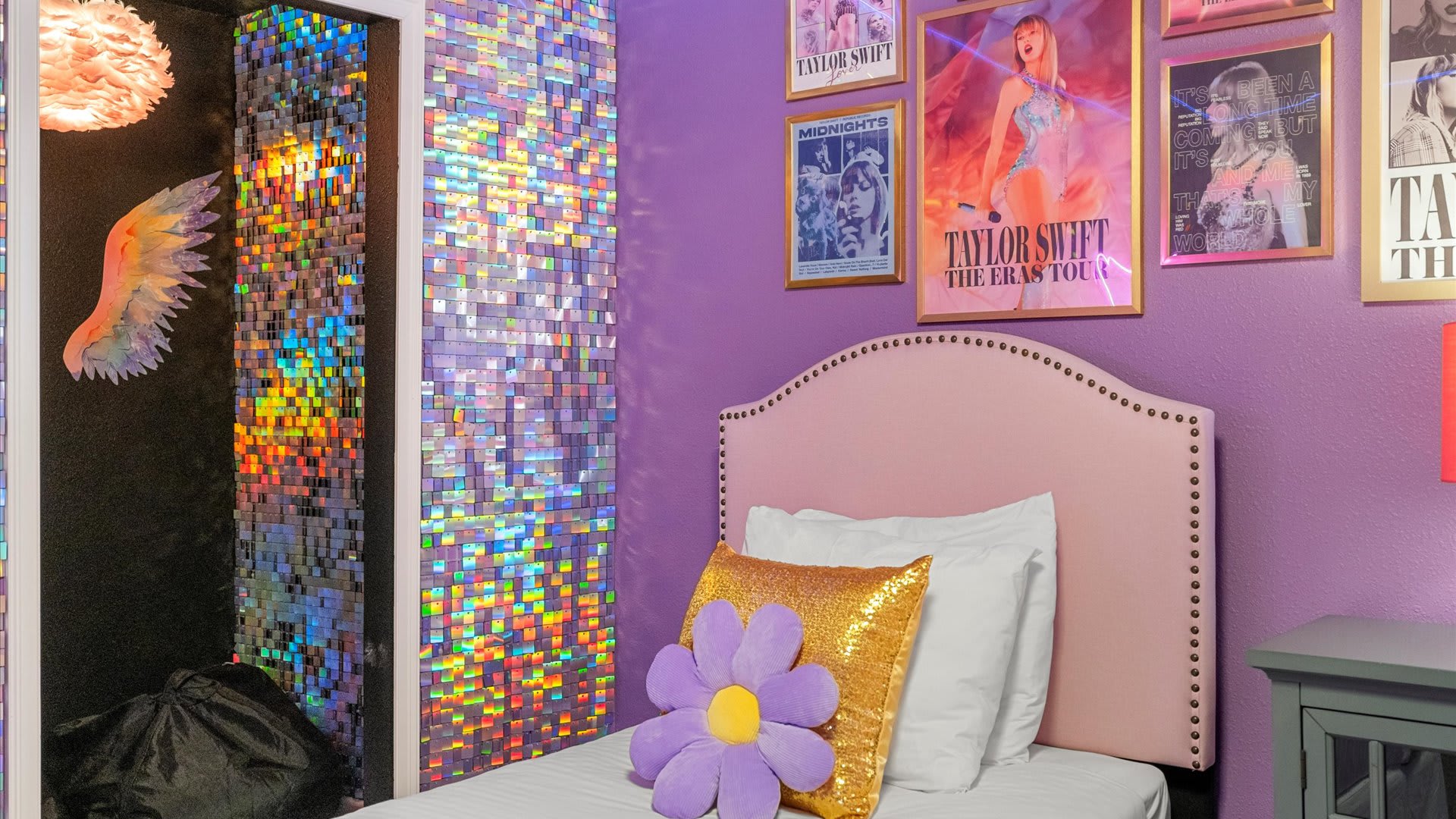 Detailed view of the Taylor Swift themed bedroom, highlighting the iridescent mirrored wall and the entrance to a closet with a unique light fixture. Pink upholstered twin beds and wall posters are also visible.