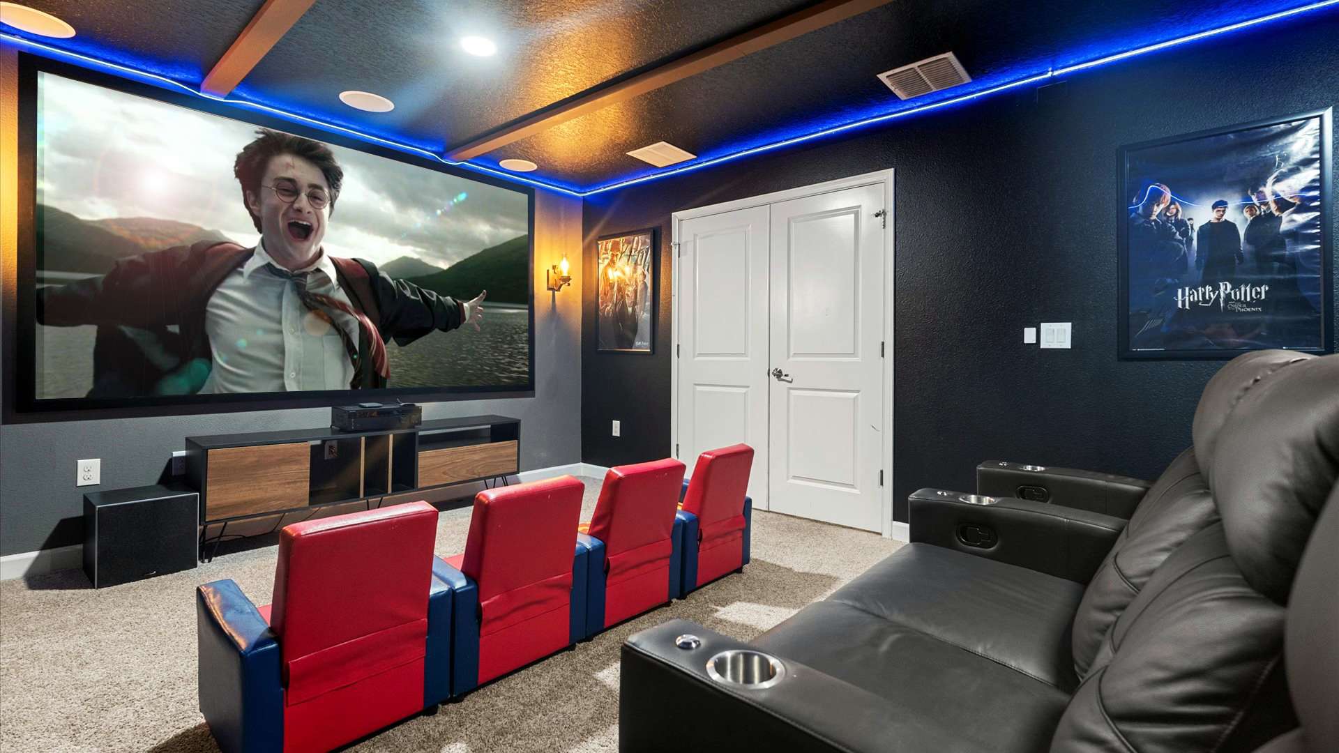 A Harry Potter-themed home cinema showcases a large projection screen with a movie scene, complemented by a row of red and blue themed chairs, black recliners, and a Harry Potter poster on the dark wall.