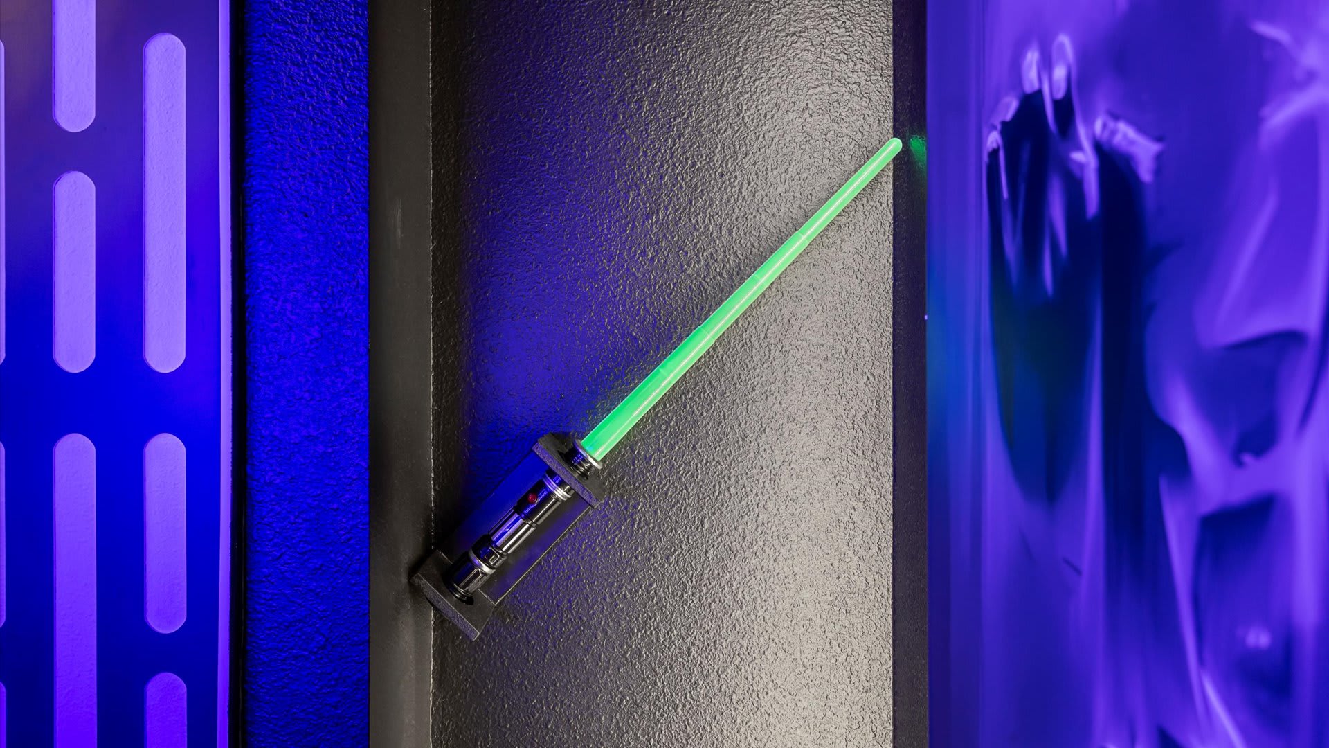 A detailed shot of a green lightsaber replica mounted on a dark wall, flanked by Star Wars-themed wall panels with blue backlighting.