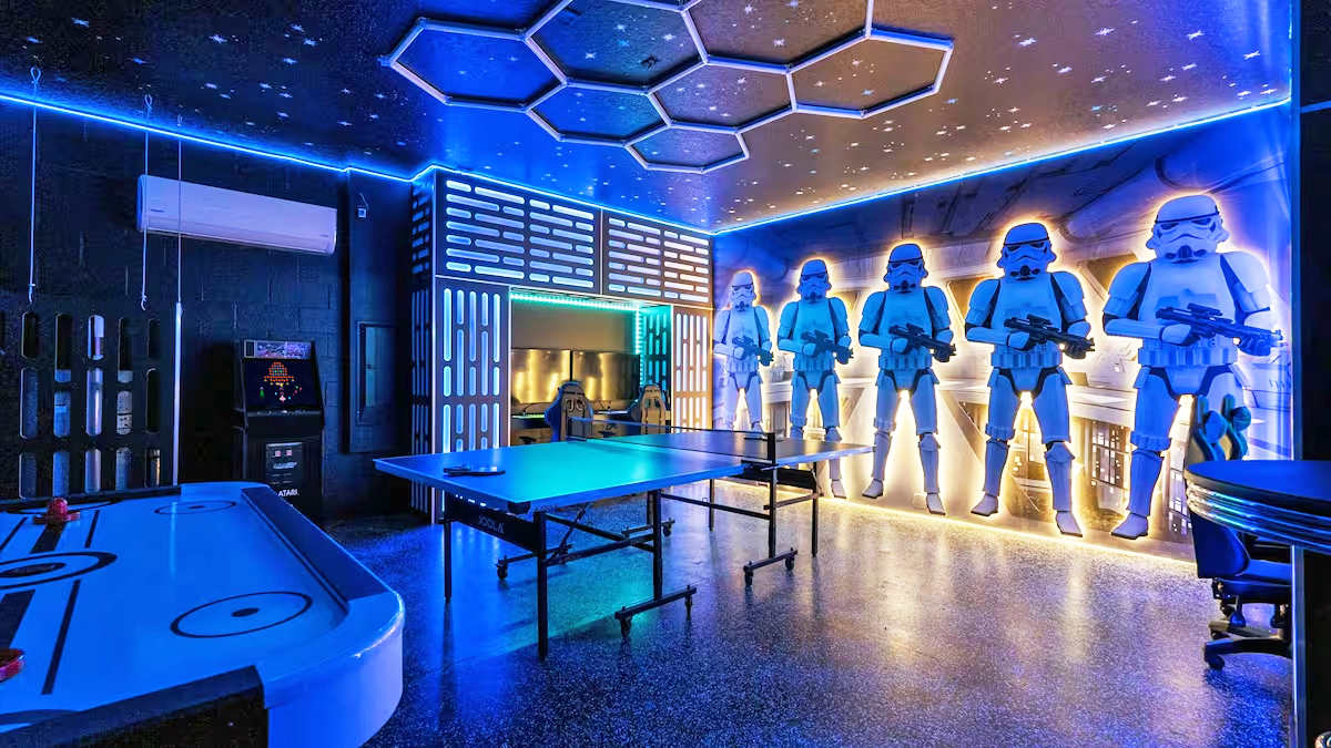 A vibrant, Star Wars-themed game room features blue LED lighting, a ping-pong table, an air hockey table, and arcade machines. Large Stormtrooper figures line one wall, and the ceiling has hexagonal light fixtures, creating an immersive entertainment space.