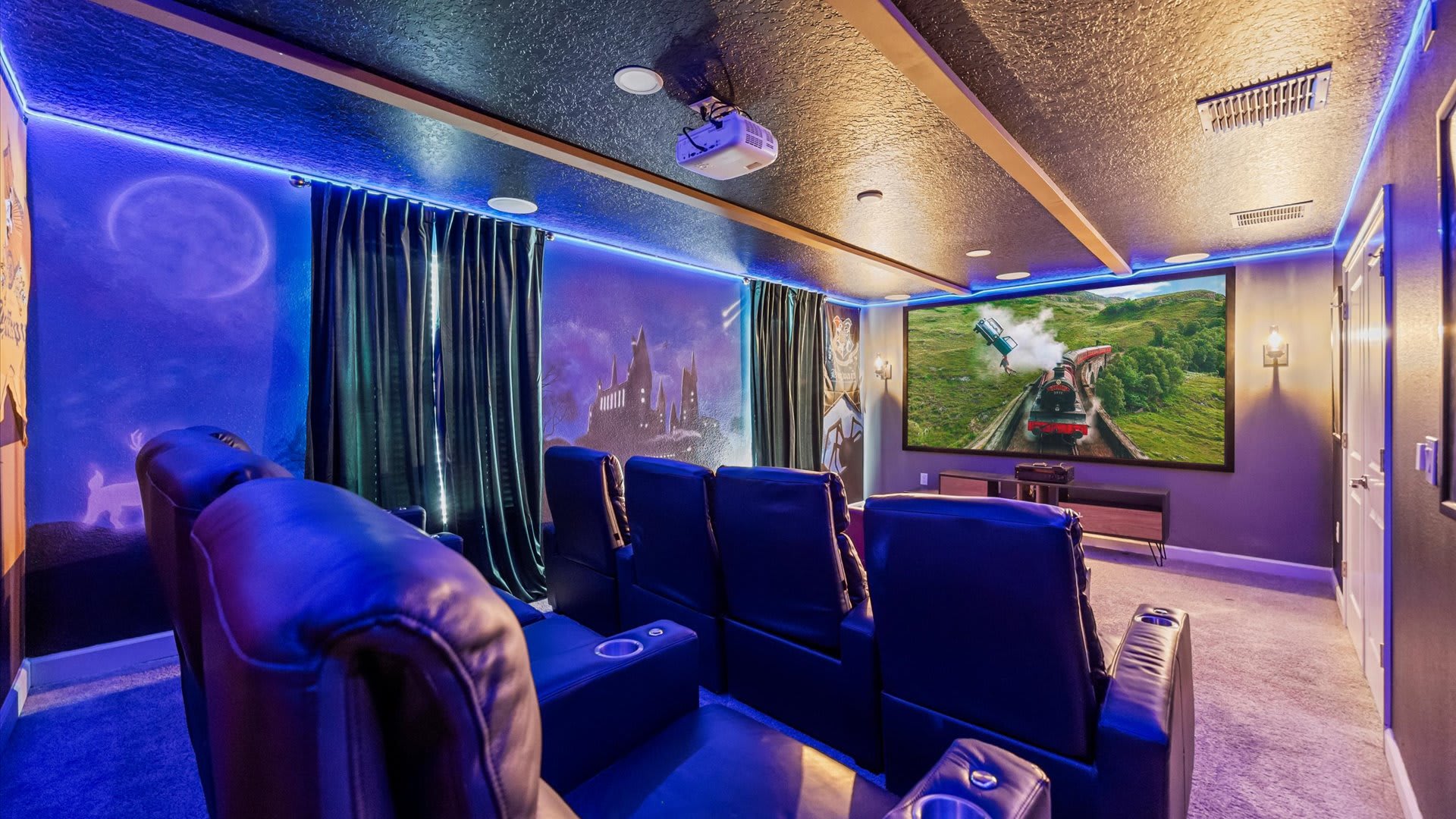 A dark, Harry Potter-themed media room features comfortable reclining theater seats facing a large projection screen displaying a movie scene. Blue LED strip lighting illuminates the walls, which are adorned with magical murals, creating an immersive cinematic experience.