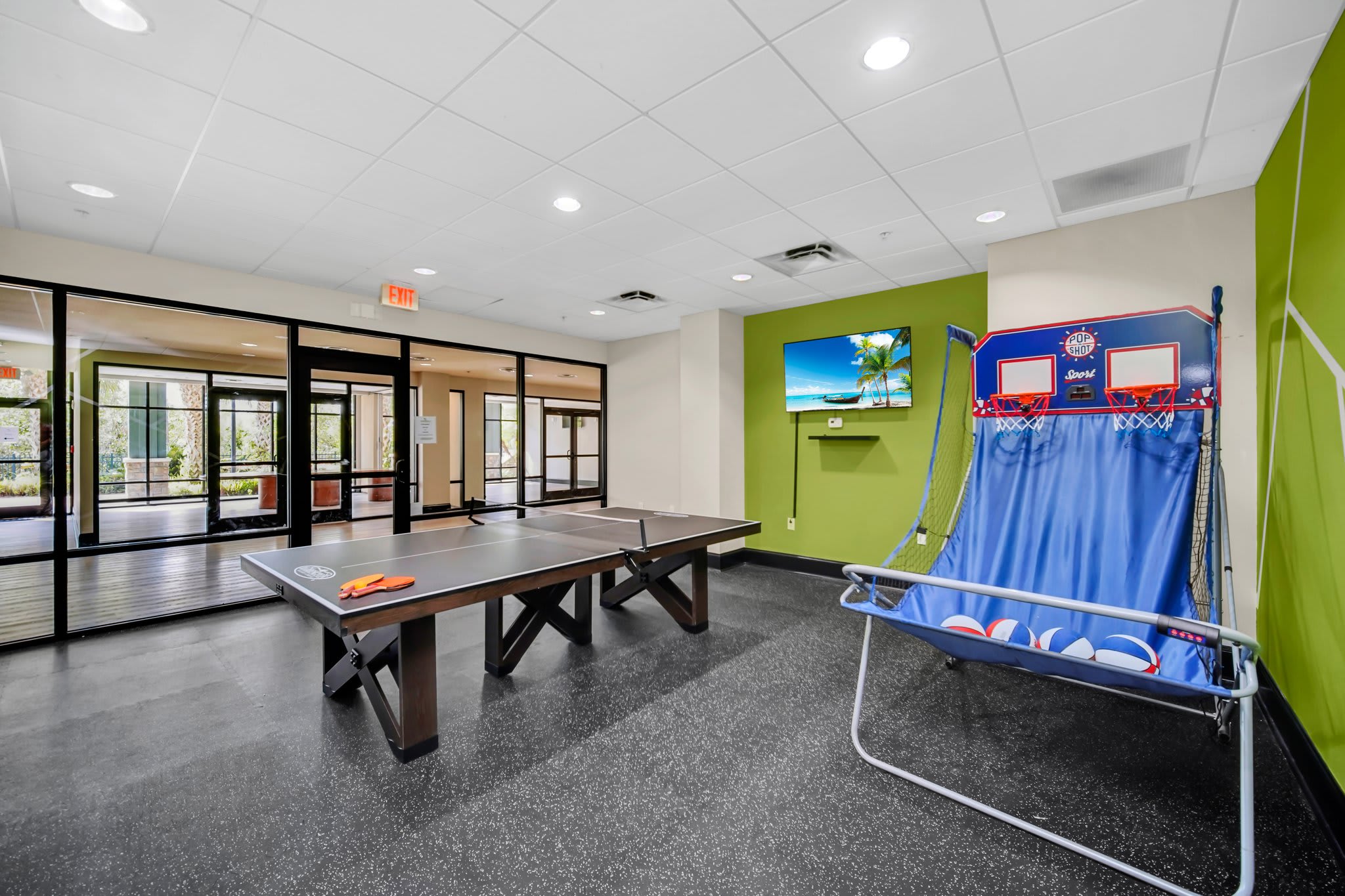 A vibrant game room equipped with a ping pong table, an arcade basketball game, and a wall-mounted flat-screen TV, featuring a green accent wall.