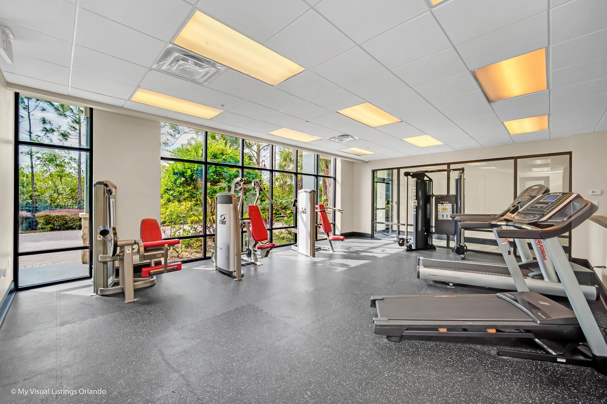 A well-equipped fitness center featuring various exercise machines including treadmills and weight stations, with large windows offering views of the surrounding greenery.