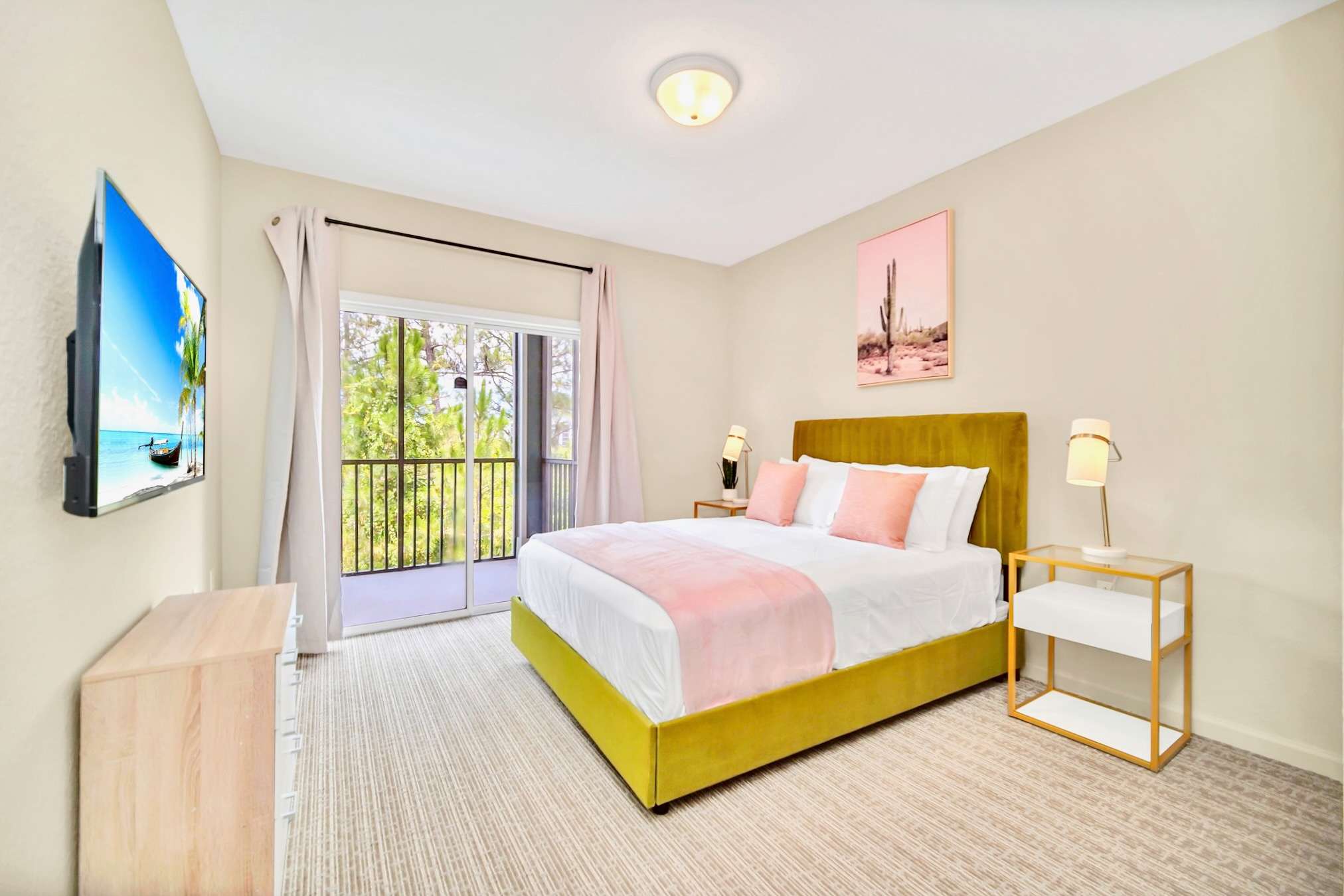 A cozy bedroom with a queen-sized bed featuring a chartreuse velvet headboard and pink accents, a wall-mounted TV, and a sliding glass door leading to a private balcony.