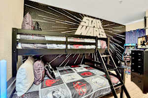 A themed children's bedroom featuring a black wooden bunk bed with Star Wars bedding and a large Star Wars mural on the wall. The room also includes a dresser and what appears to be an arcade game in the background, creating a fun and engaging space.