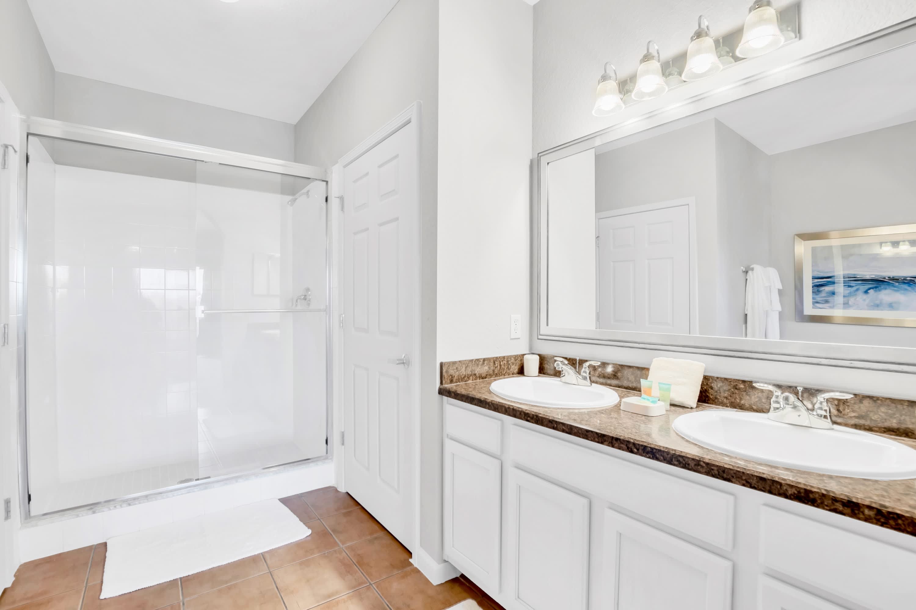 Modern bathroom with a double vanity featuring two sinks and a large mirror, alongside a spacious walk-in shower with a glass enclosure and tiled walls.