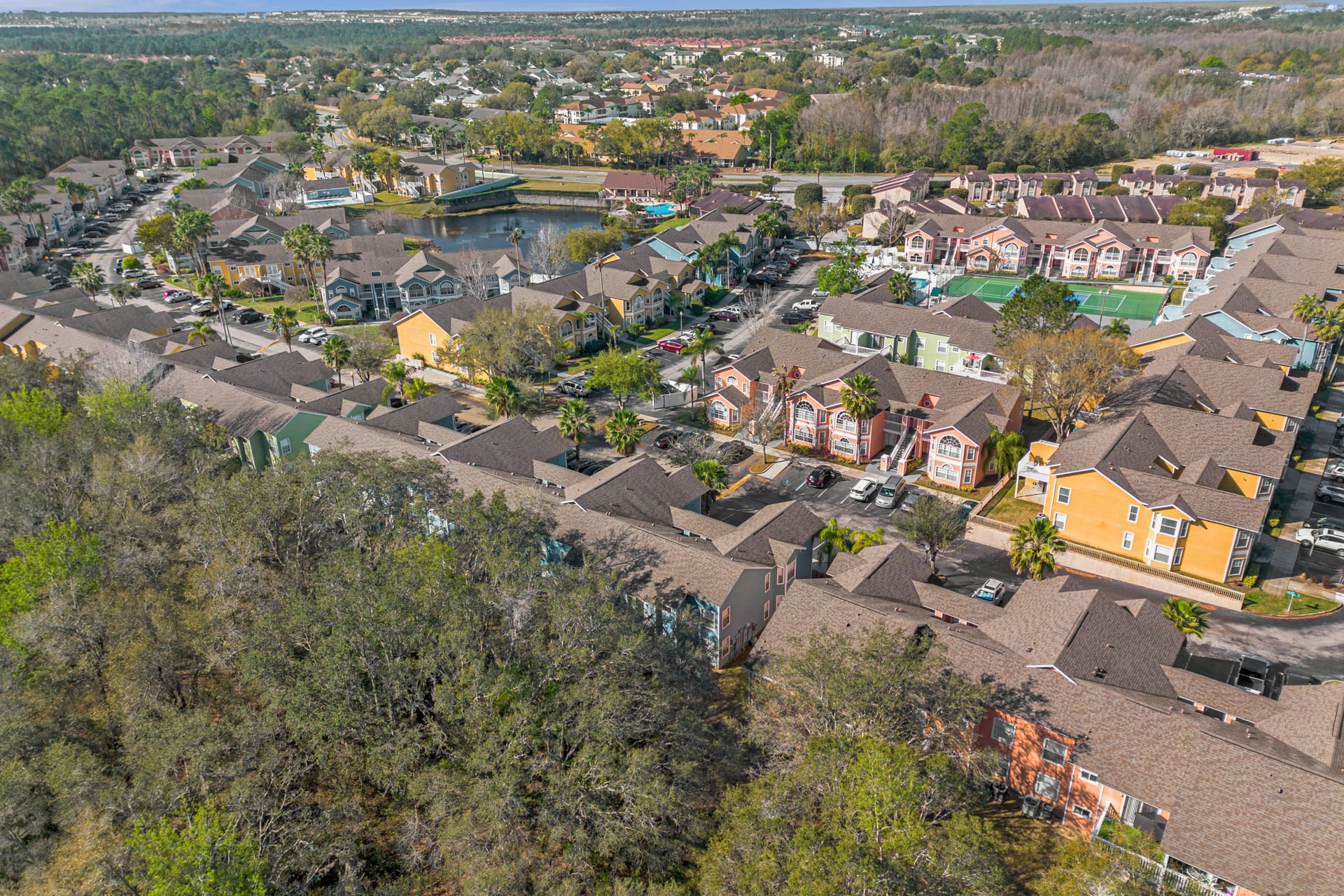 A broad aerial shot revealing a large, vibrant resort community with numerous colorful condominium buildings, lush green landscaping, and a central pond, all interconnected by roads and parking lots.