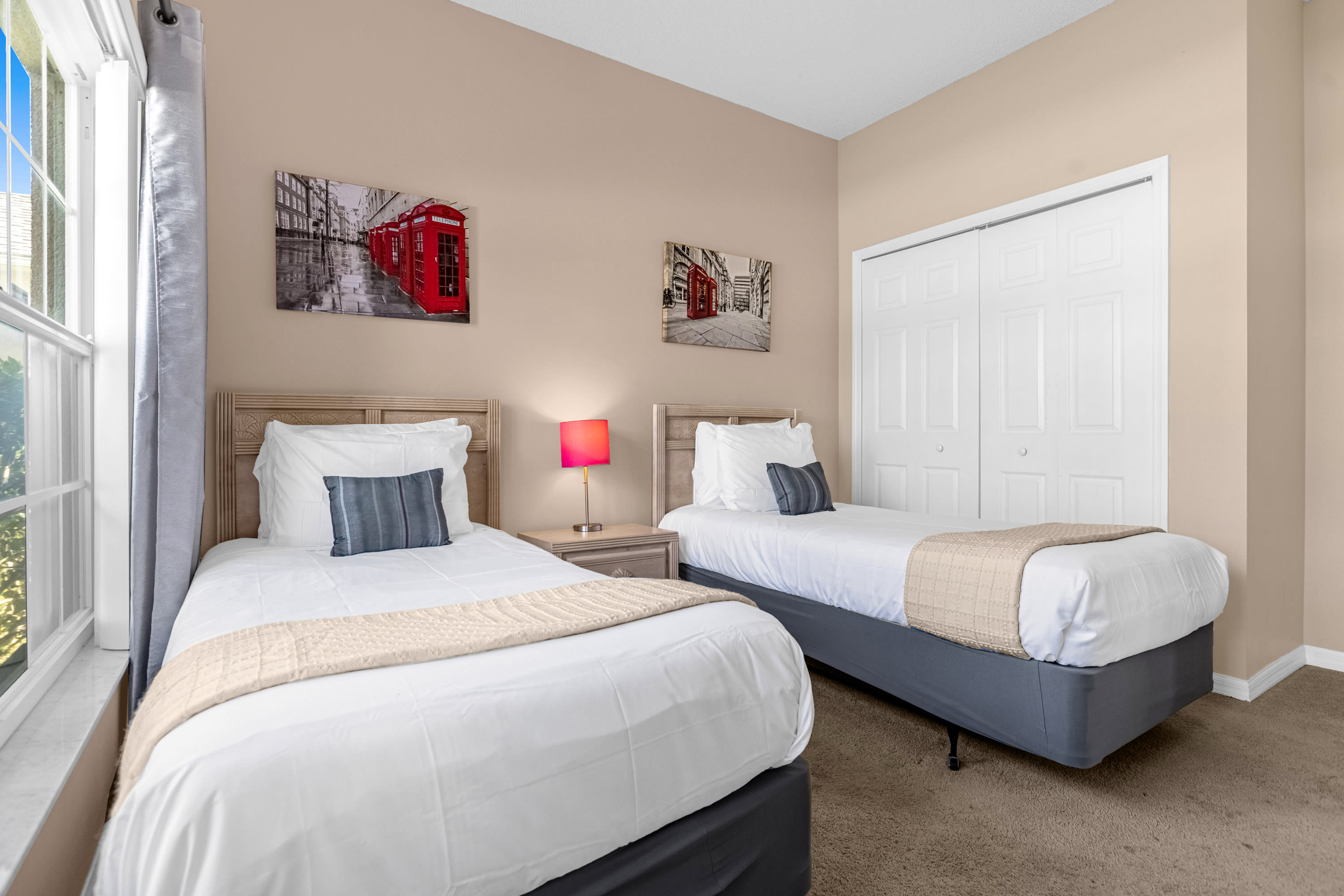 Another view of the twin bedroom, showcasing two beds with light wood headboards and white bedding, along with two London-themed wall art pieces. A white bi-fold closet door is visible on the right.