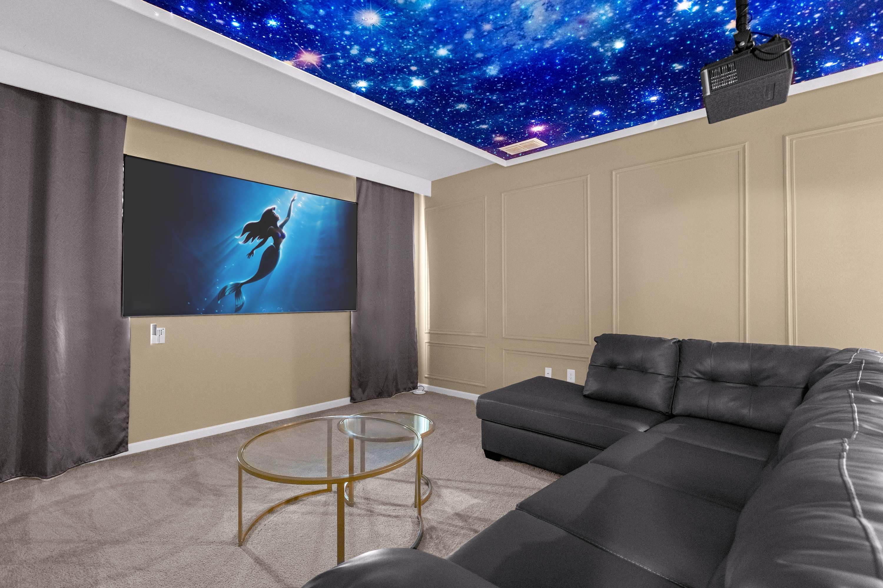 A cozy media room features a large projection screen displaying a mermaid image, with a comfortable black sectional sofa and two round glass coffee tables. The ceiling is adorned with a starry night sky mural, enhancing the immersive viewing experience.