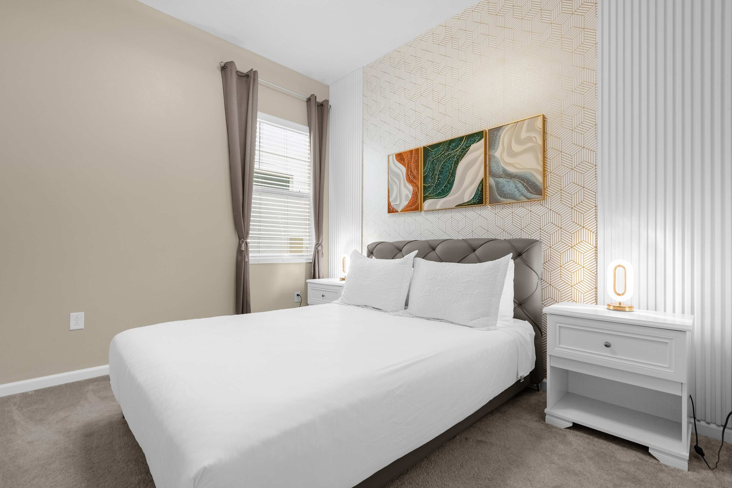 Elegant bedroom with a queen-sized bed, two white nightstands with modern lamps, and decorative wall art above a textured headboard, set against a geometric patterned accent wall.