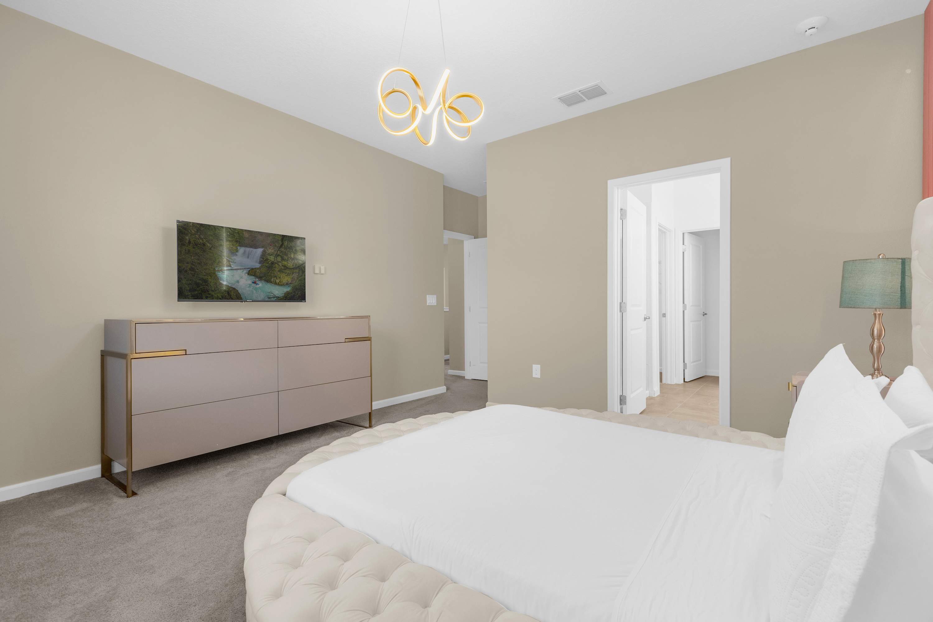 View of the elegant bedroom showing the round bed, a modern light pink dresser with gold accents, and a wall-mounted TV displaying a nature scene.