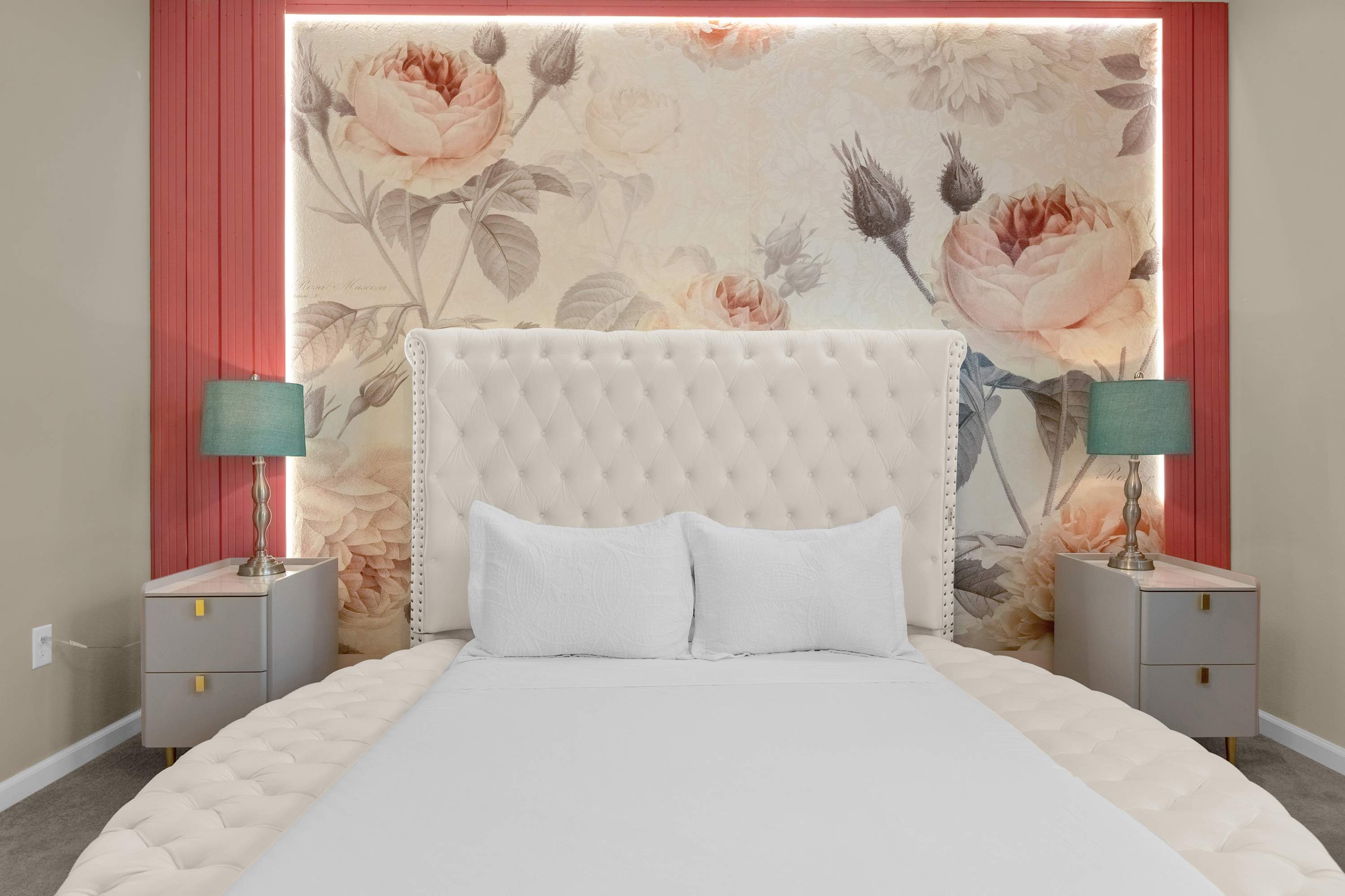 Close-up of the luxurious tufted round bed with white bedding, flanked by two nightstands with teal lamps, set against a floral accent wall with vertical pink paneling.